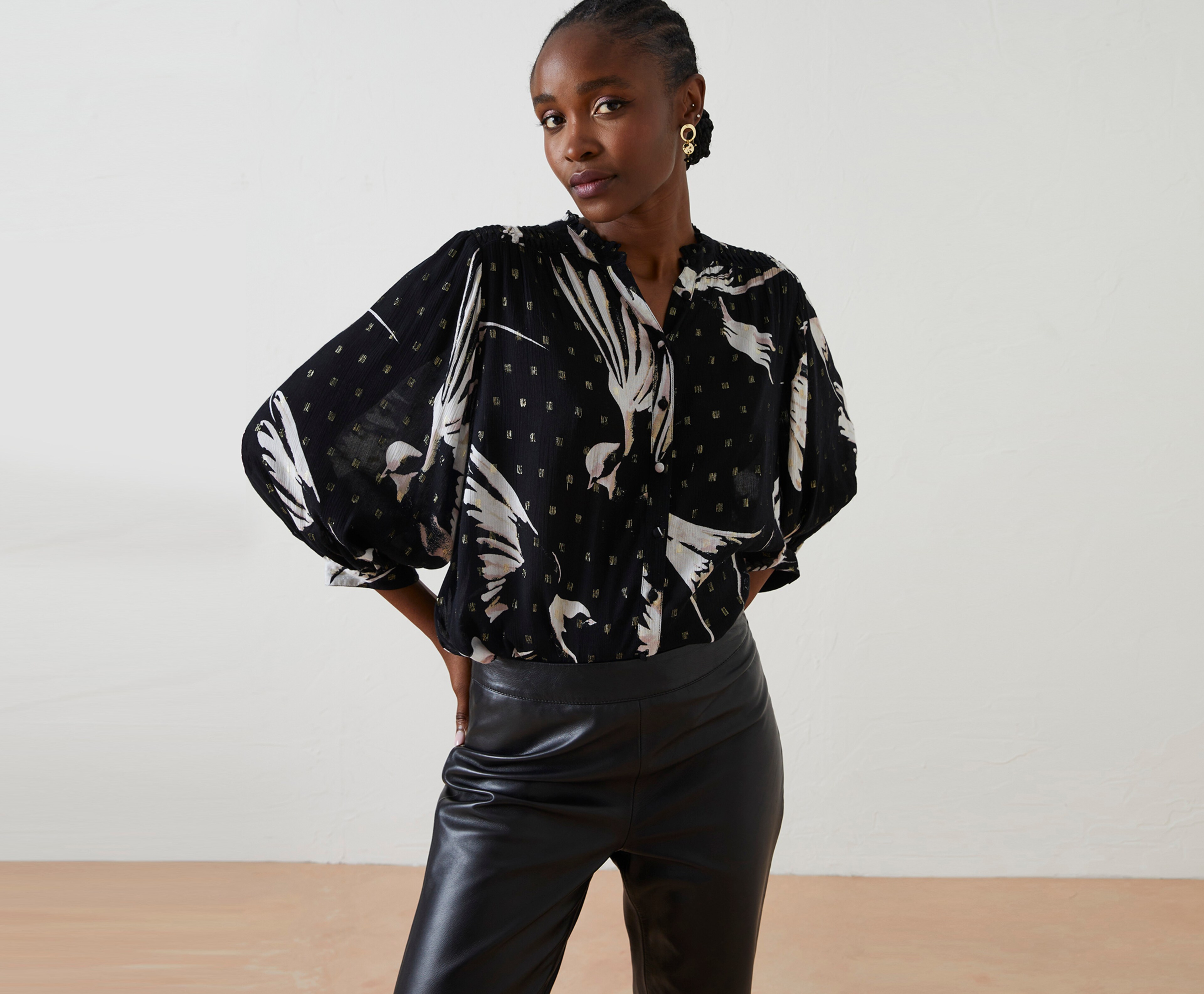 Woman stood in a patterned black blouse and faux leather trousers