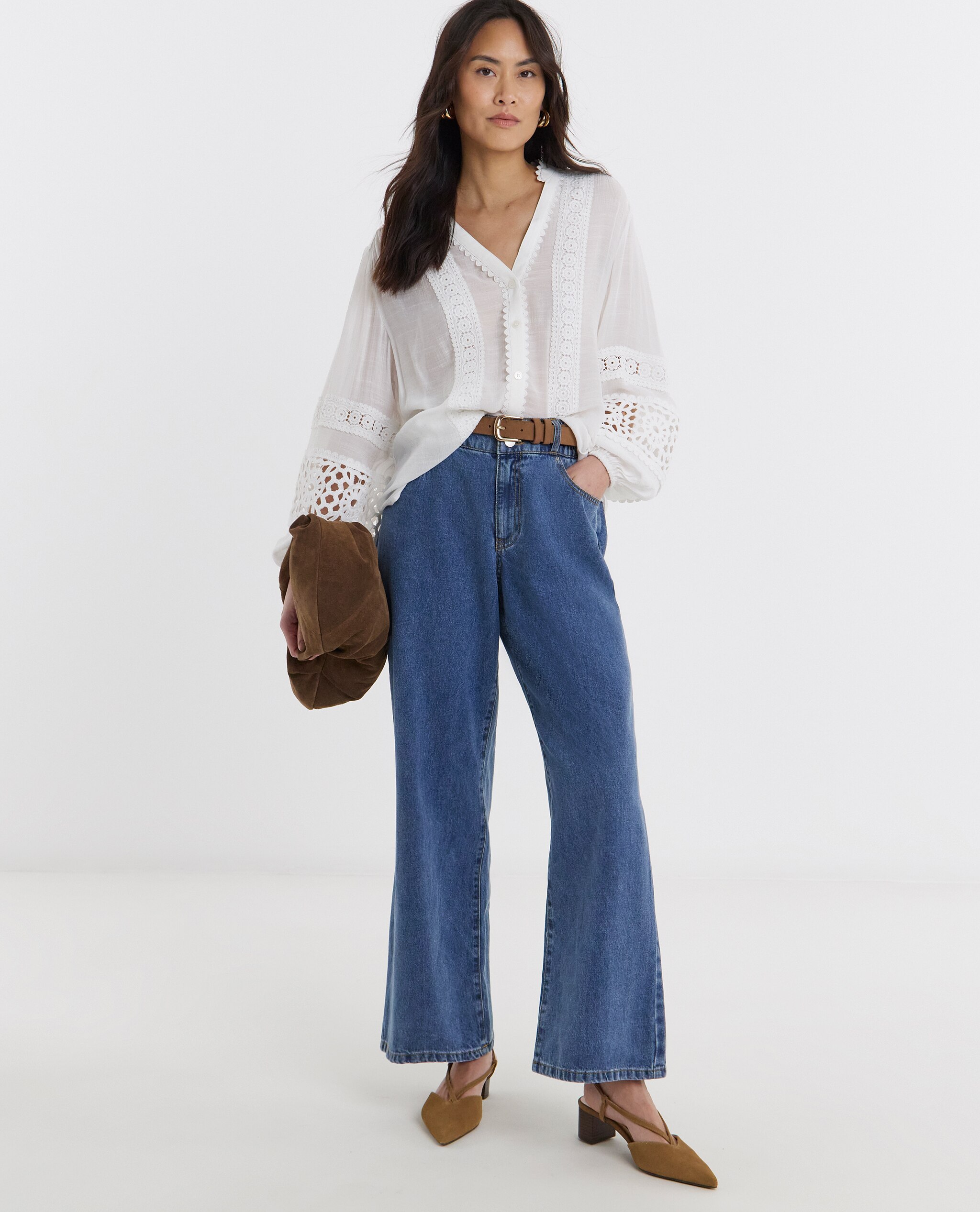 Model is wearing a lace trim button through prairie blouse with blue denim jeans and a tan belt and camel low heel pointed toe leather slingback shoes.