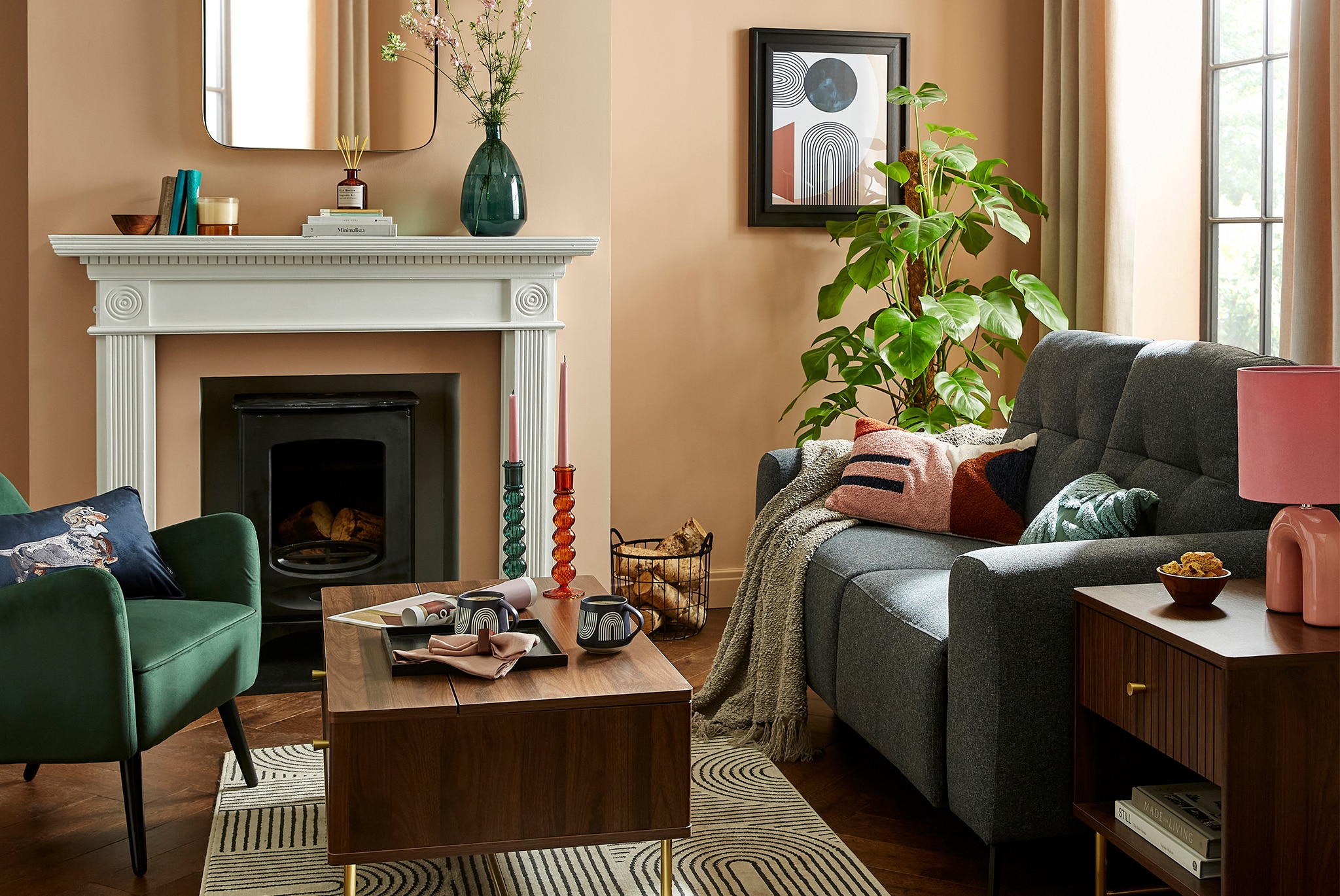 A stylish living room with a sofa, armchair, coffee table and fireplace, decorated with plants, candles and colourful cushions.