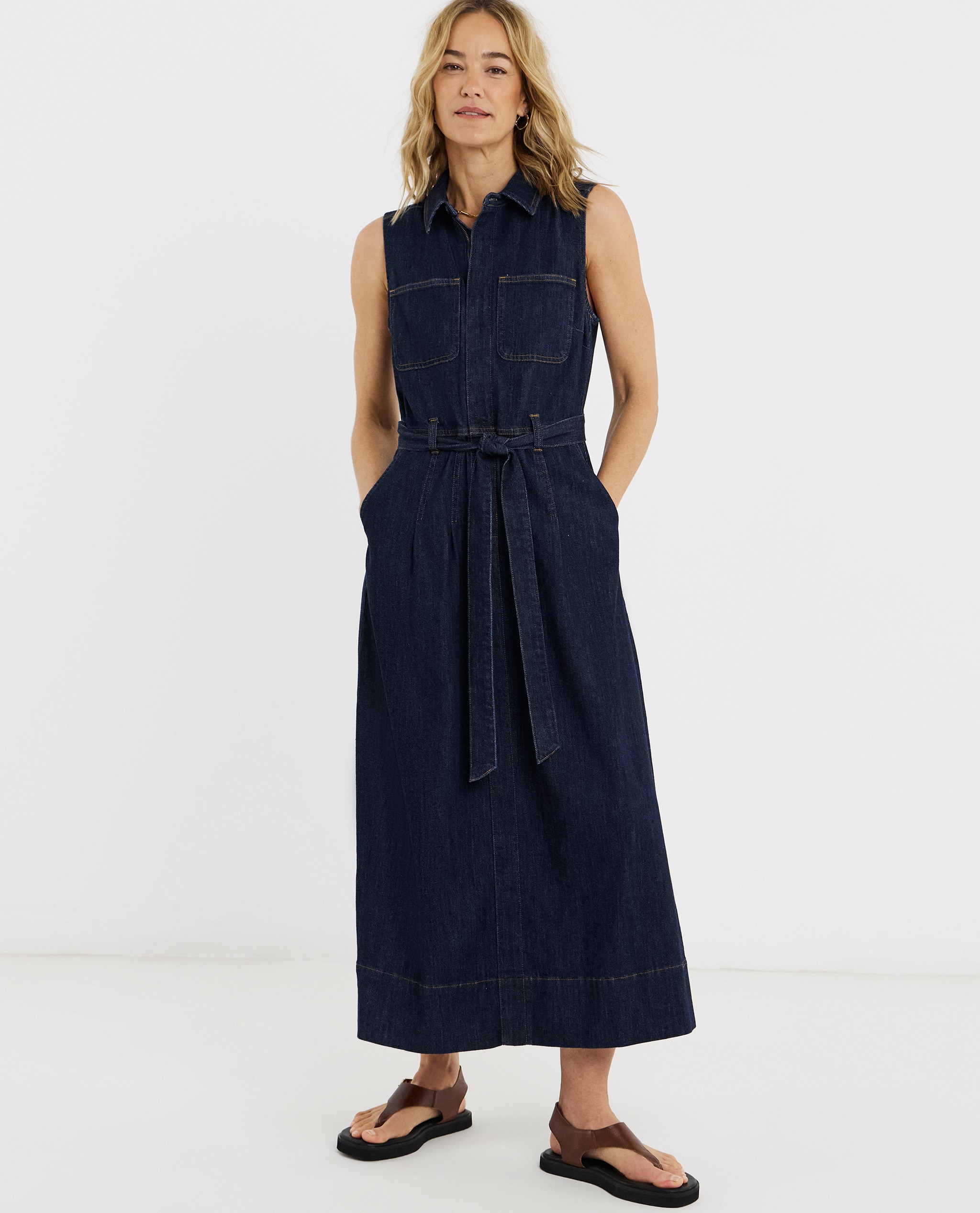 Model is wearing a indigo sleeveless pocket front midaxi dress with a pair of toe post sandals.