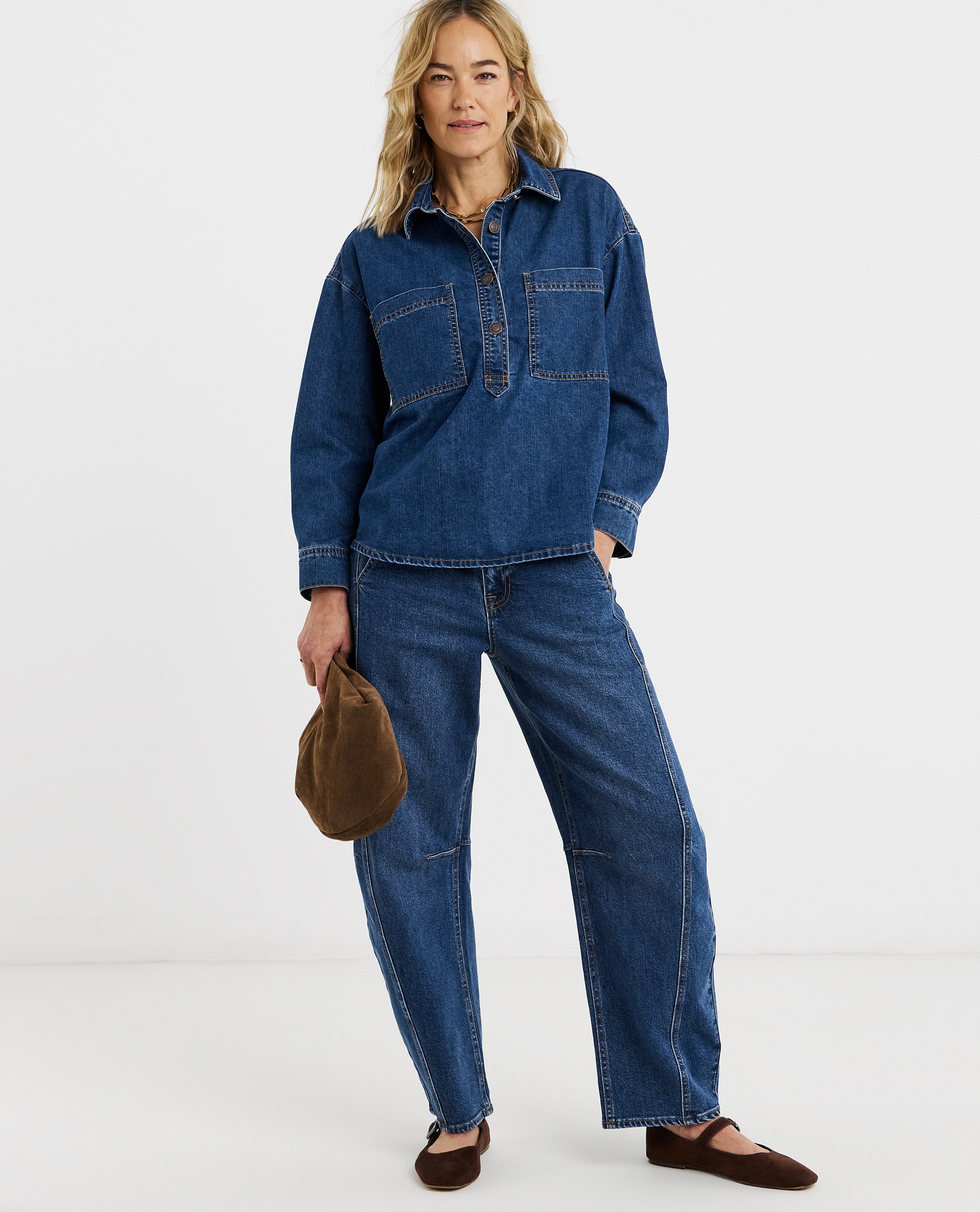 Model is wearing a dark blue denim polo shirt with dark blue barrel denim jeans and a pair of ballet flats and handbag.