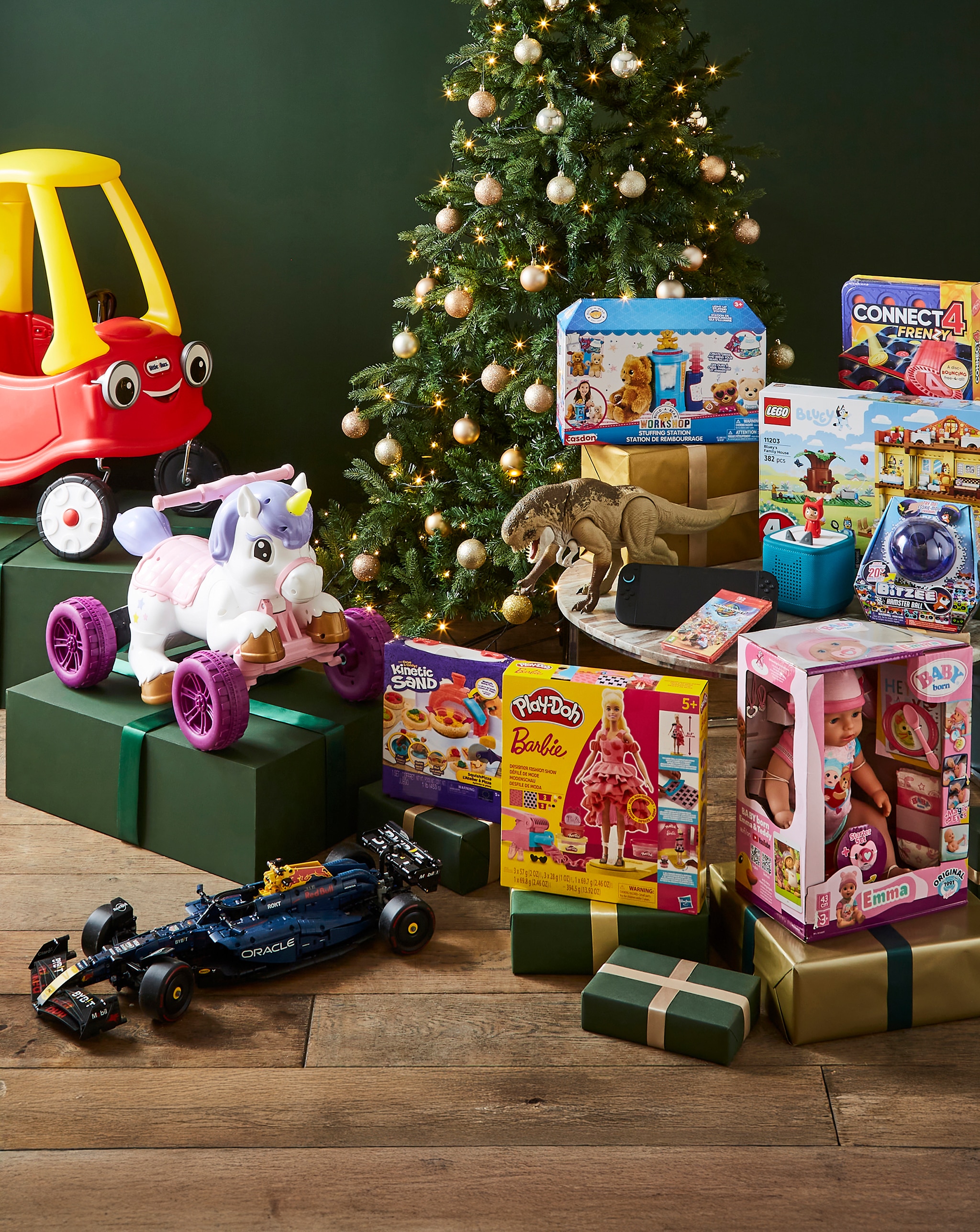 Christmas tree surrounded by wrapped gifts and various toys, including a ride-on car, unicorn scooter, and boxed play sets.