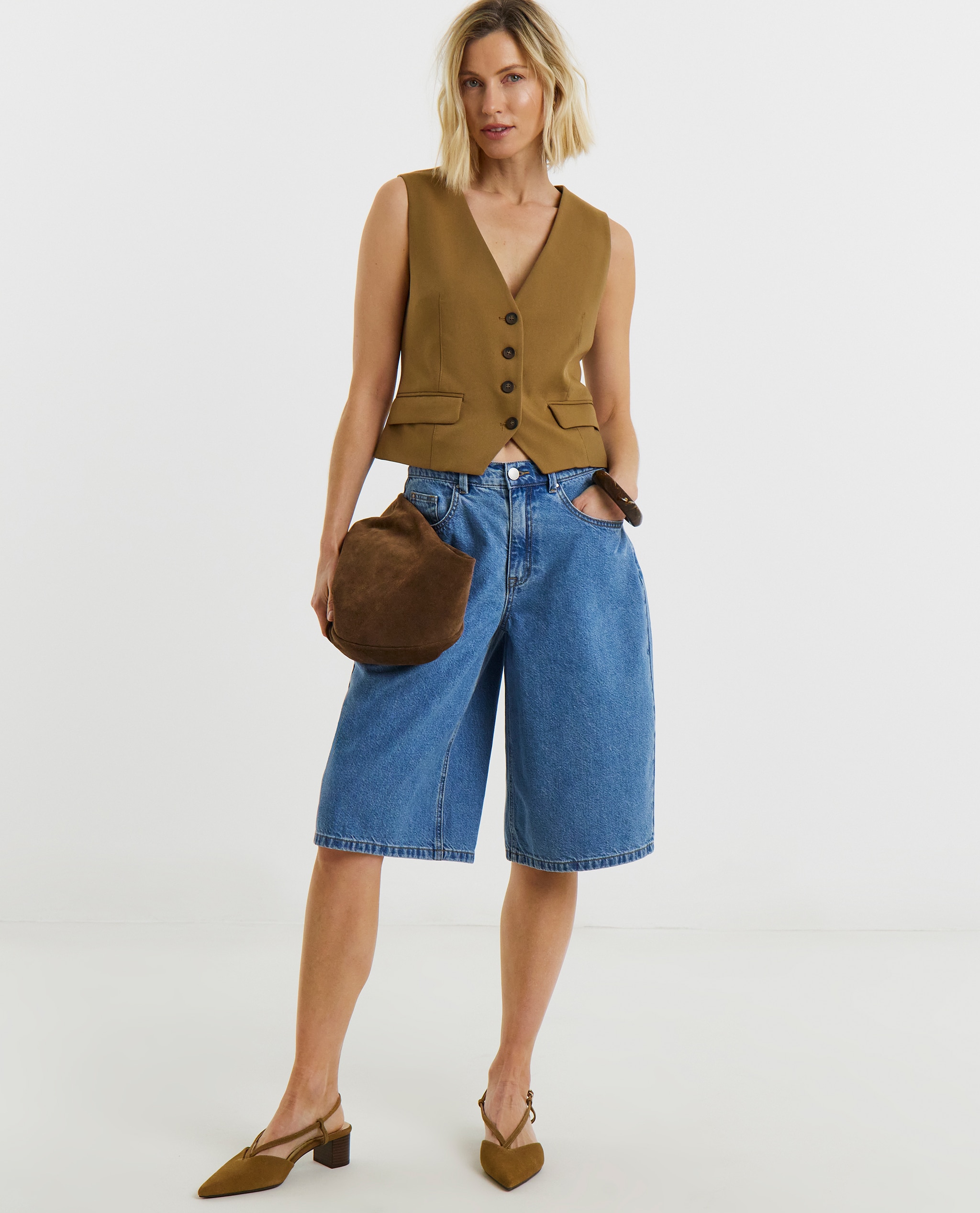 Model is wearing a camel twill waistcoat with mid blue denim jorts with low heel pointed toe leather slingback shoes in camel.