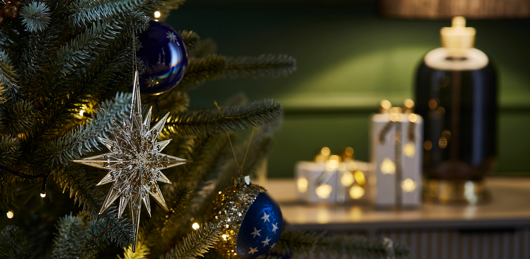 A close up of a Christmas tree in a living room with a green and blue colour theme.