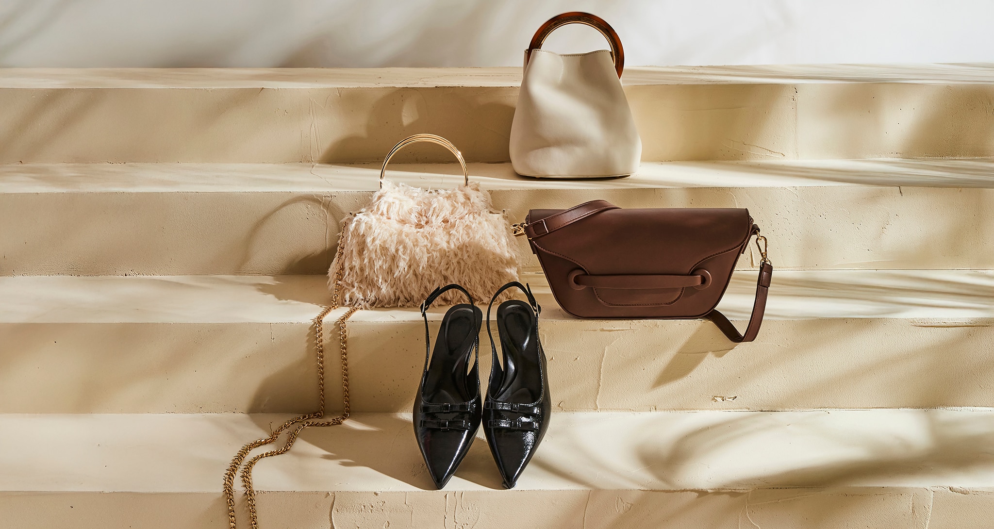 A range of accessories on some steps. 3 hand bags and a pair of black heels.