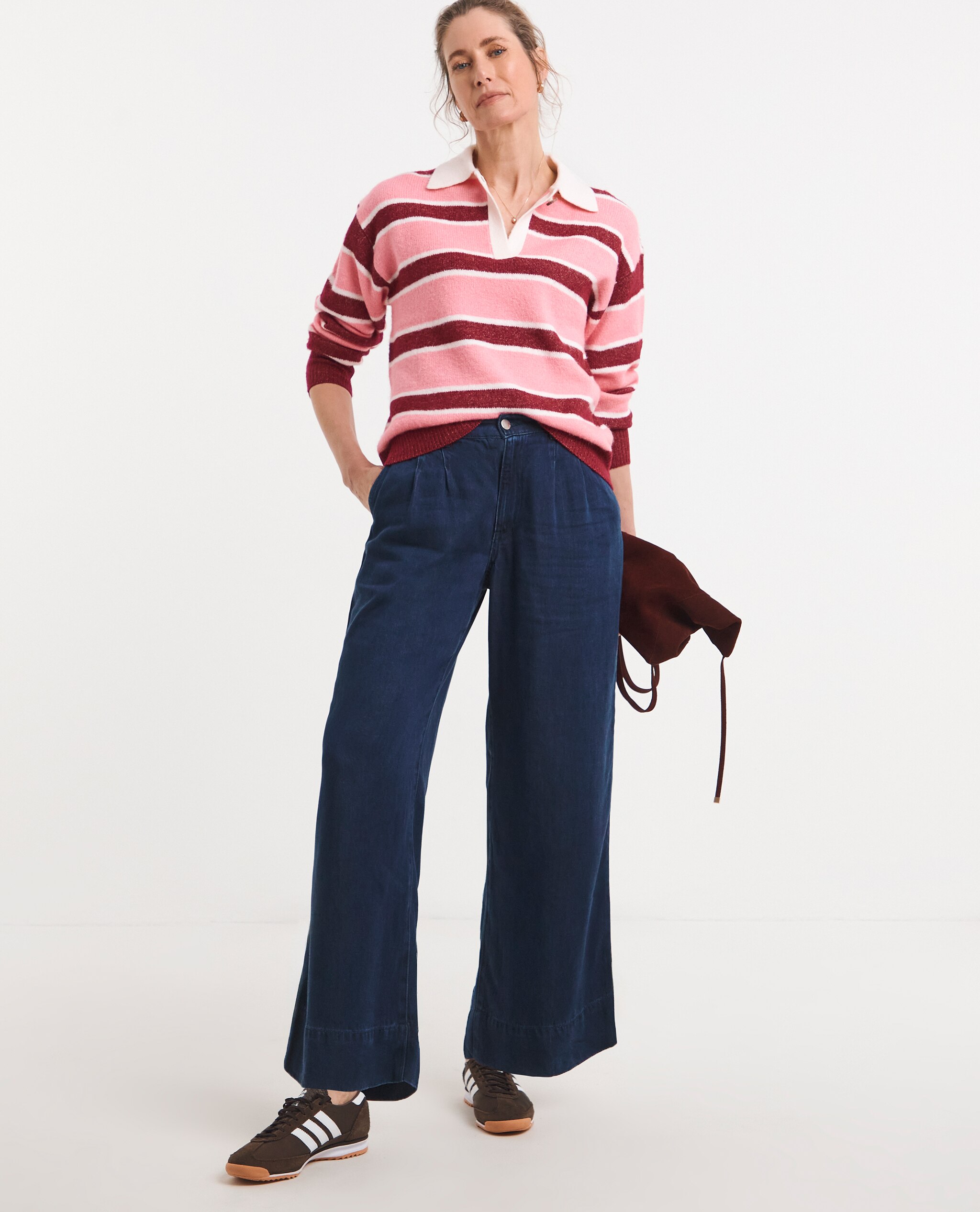 Model is wearing a stripe knitted rugby jumper with a pair of dark blue trousers.