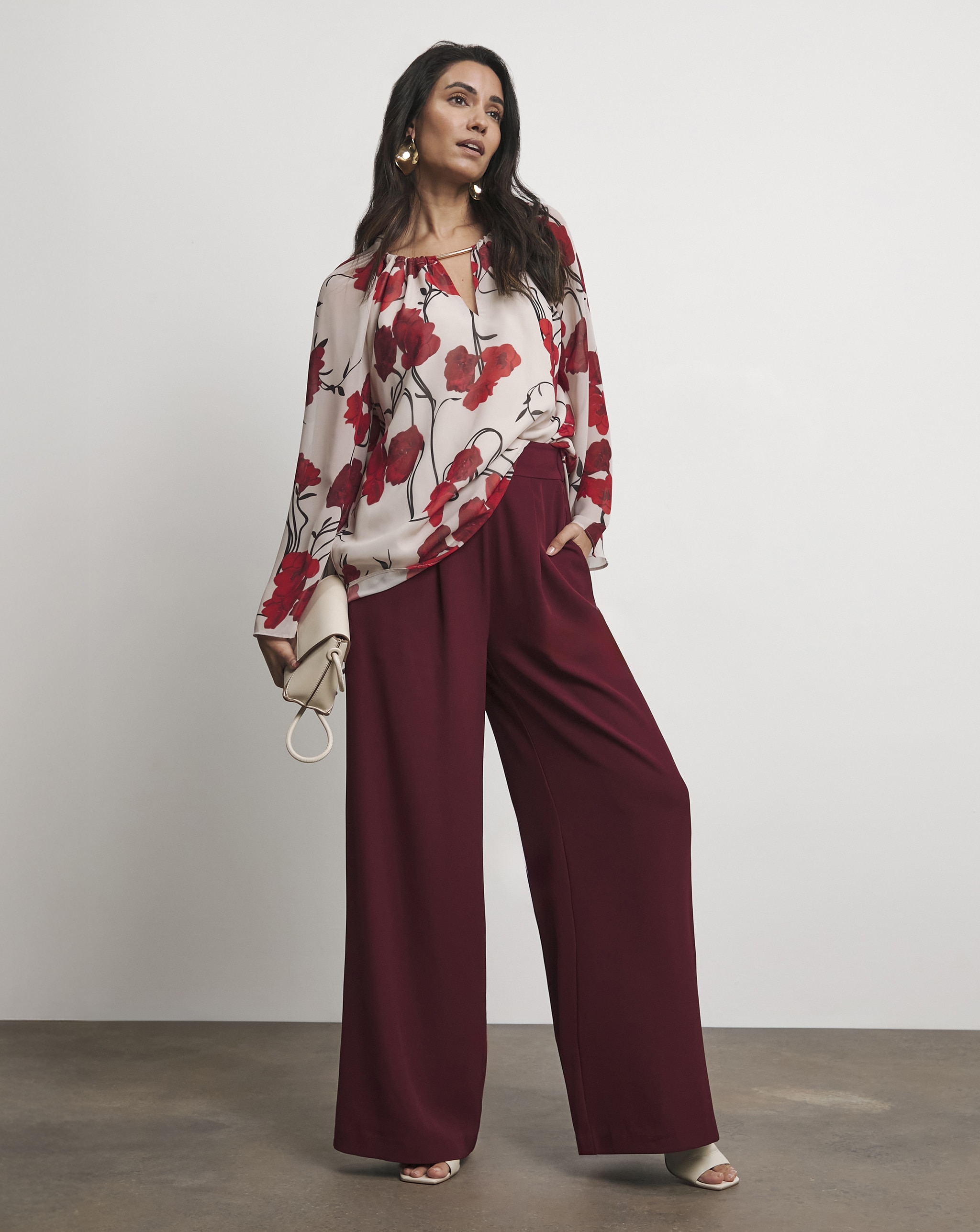 A lady stood up wearing maroon coloured wide leg trousers.