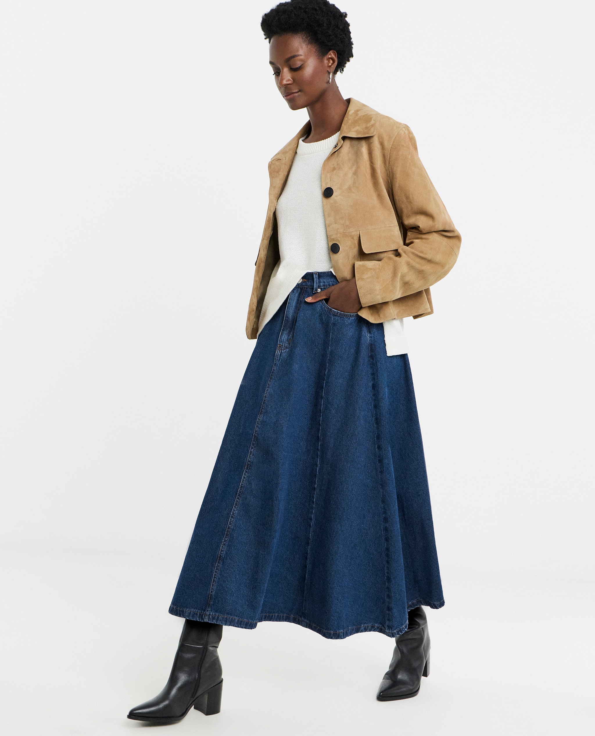 Model is wearing a camel suedette jacket with a white jumper ad a mid blue denim full circle skirt with black boots.