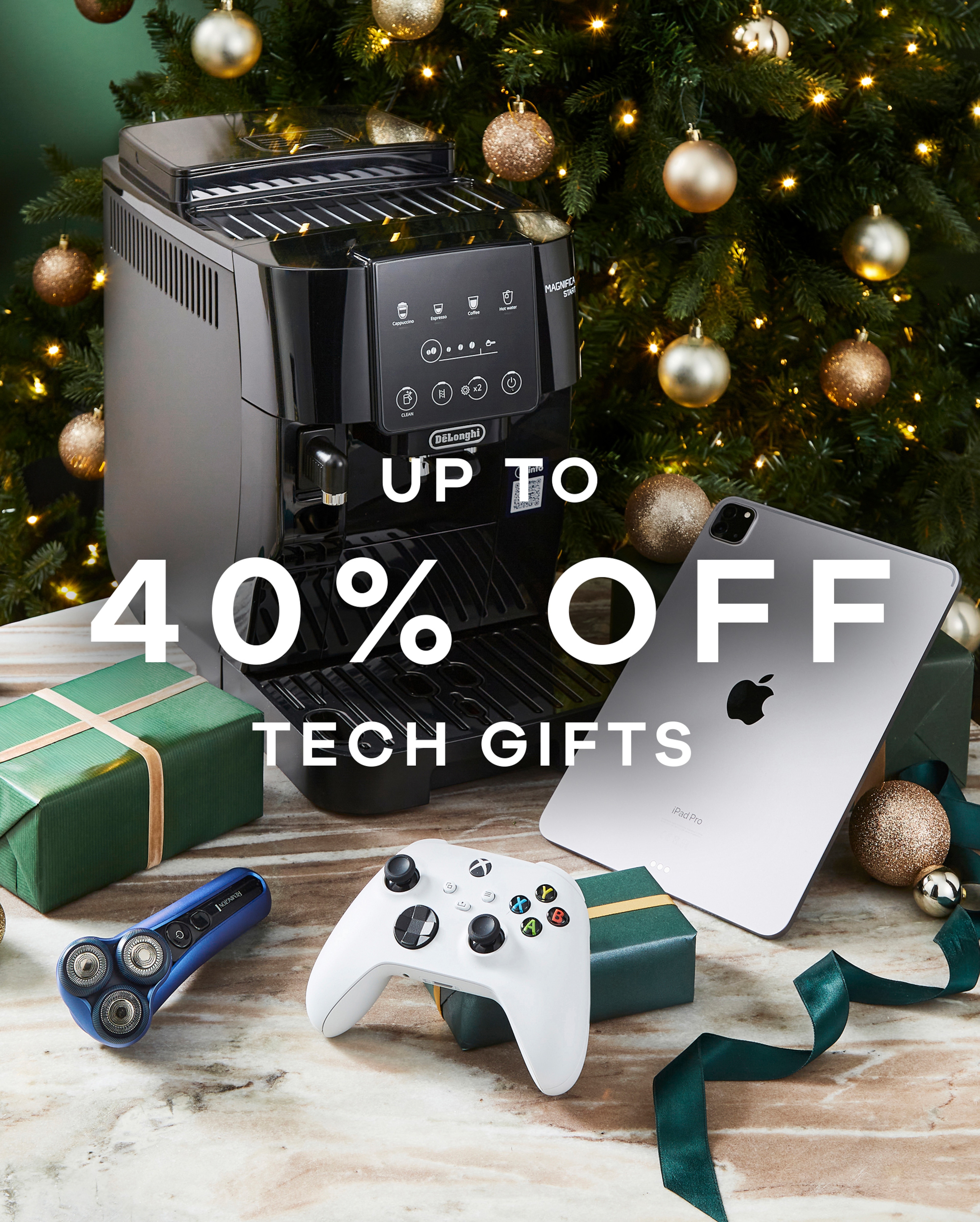 Up to 40% off tech gifts text overlaid on an image of tech goods on a table with a Christmas tree in the background.