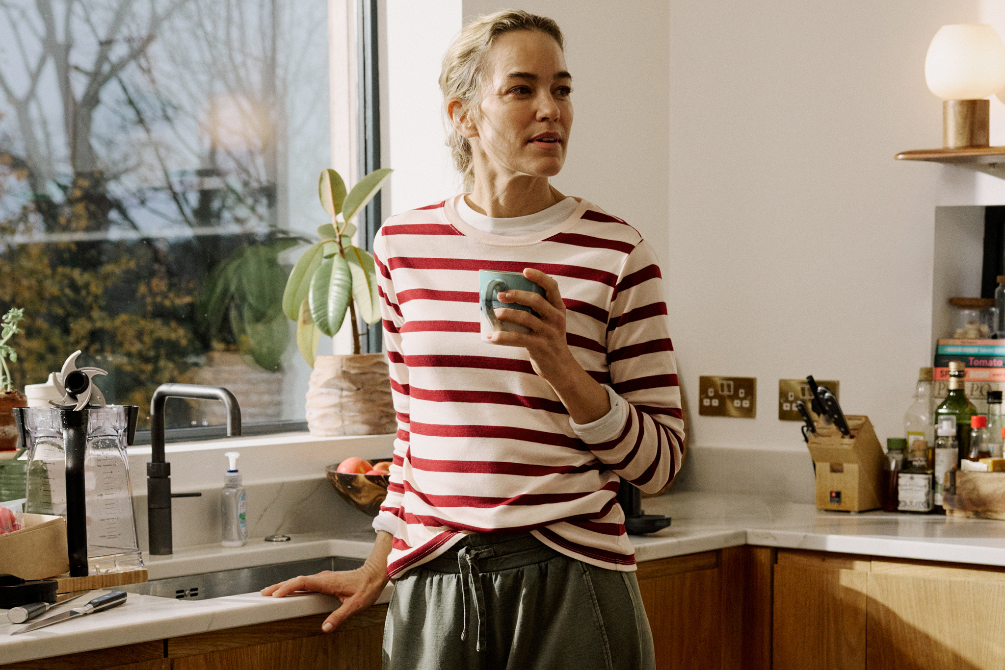 A lady inside in a kitchen wearing a white and red hooped top.