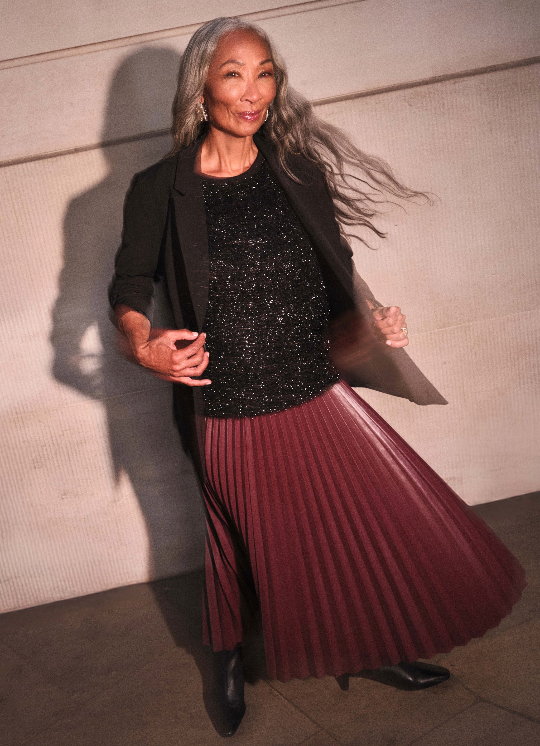 Lady stood outside wearing a pleated burgundy dress with a black sparkly top and blazer