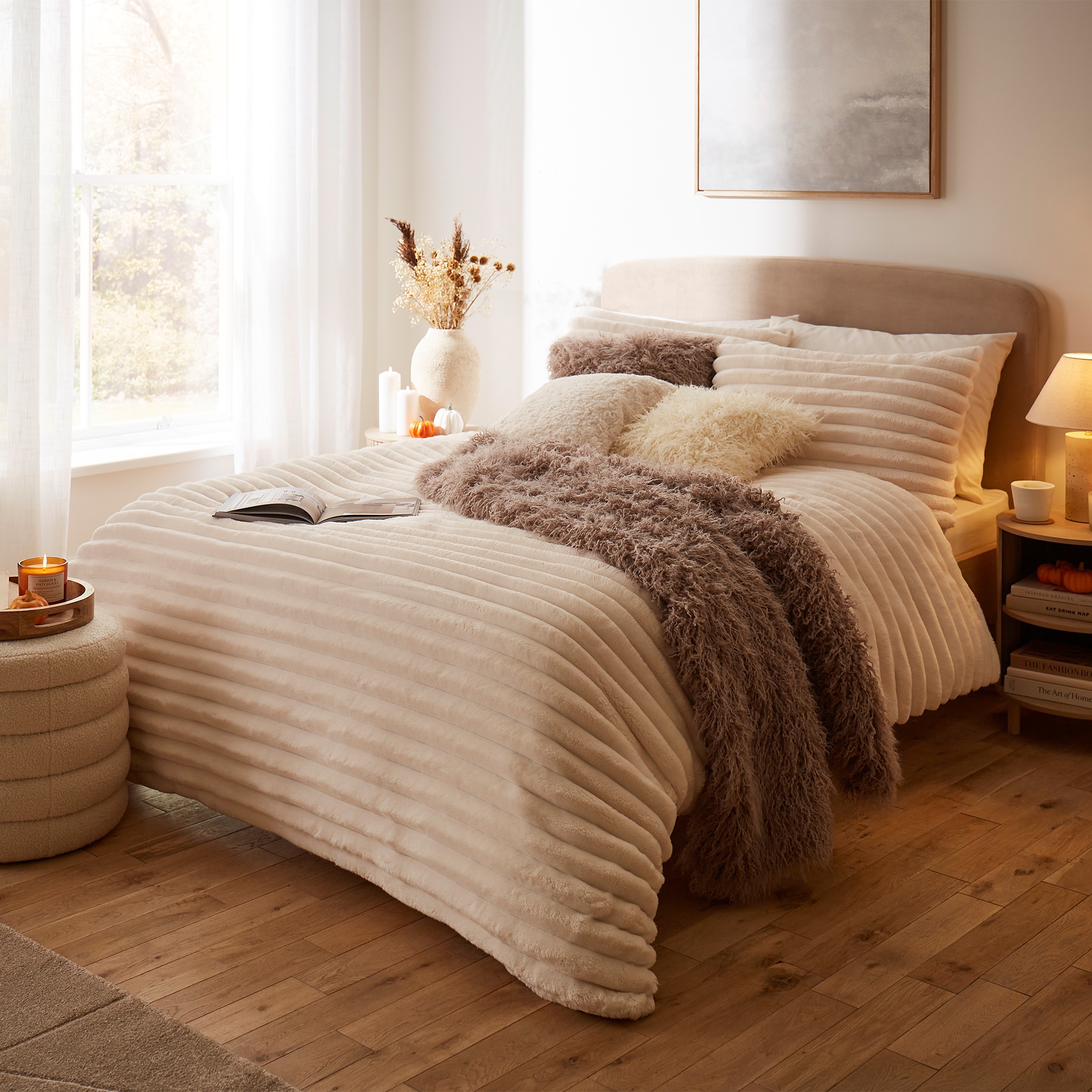 Cosy bedroom with a striped duvet, fluffy throws, cushions, and warm lighting.
