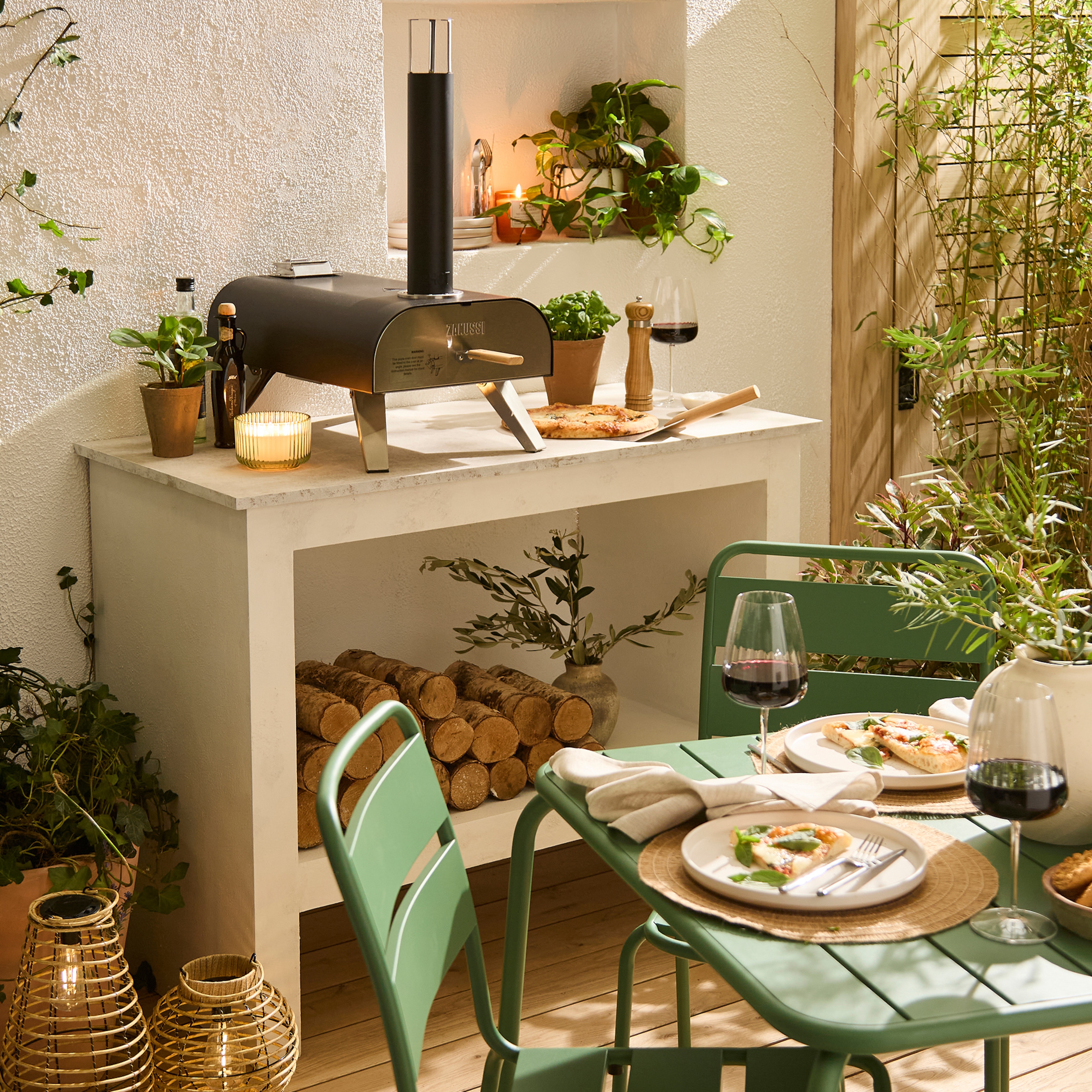 A back garden scene with green patio furniture and a pizza oven on a table.