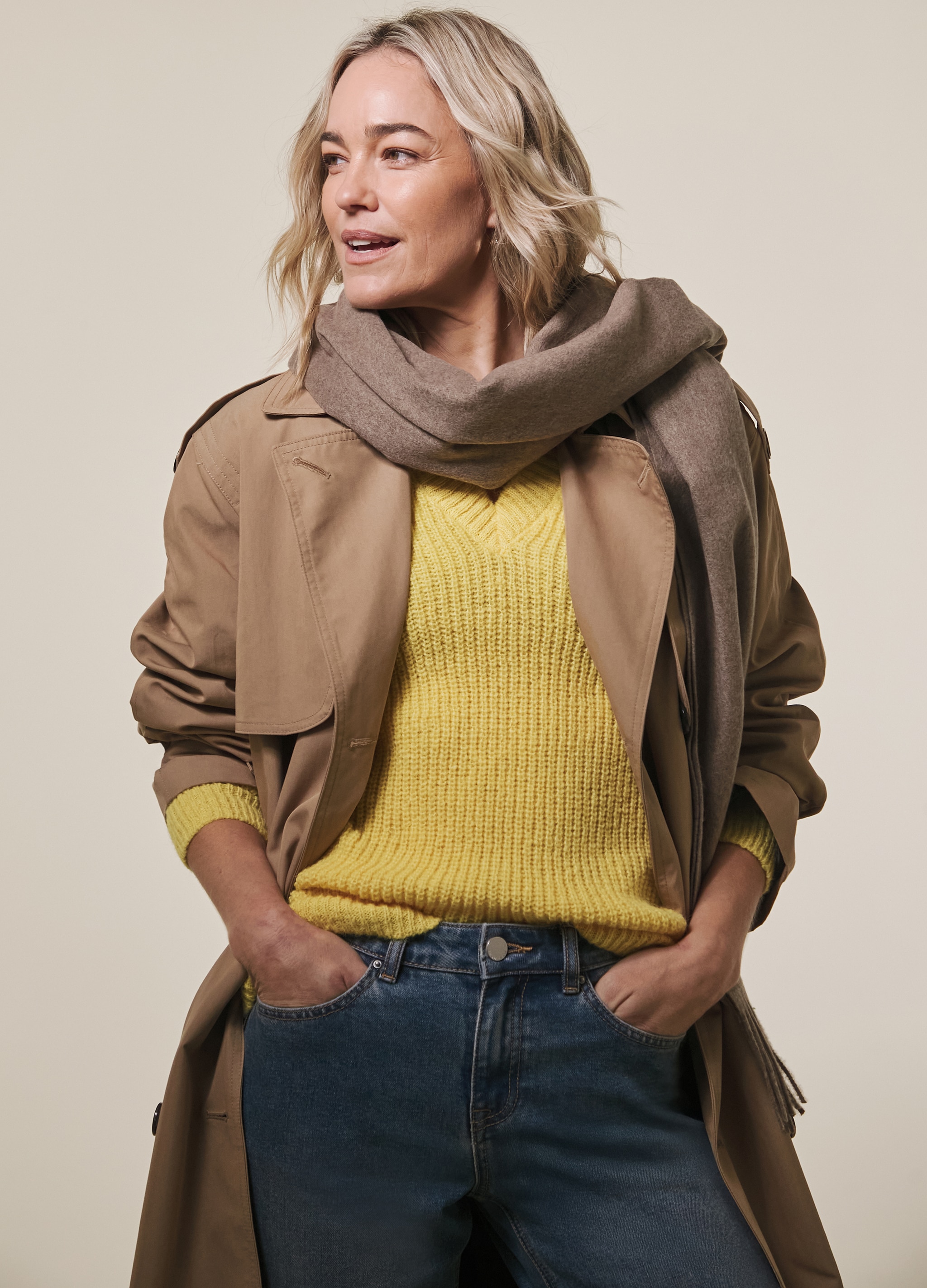 Lady wearing a light brown trench coat and a yellow jumper