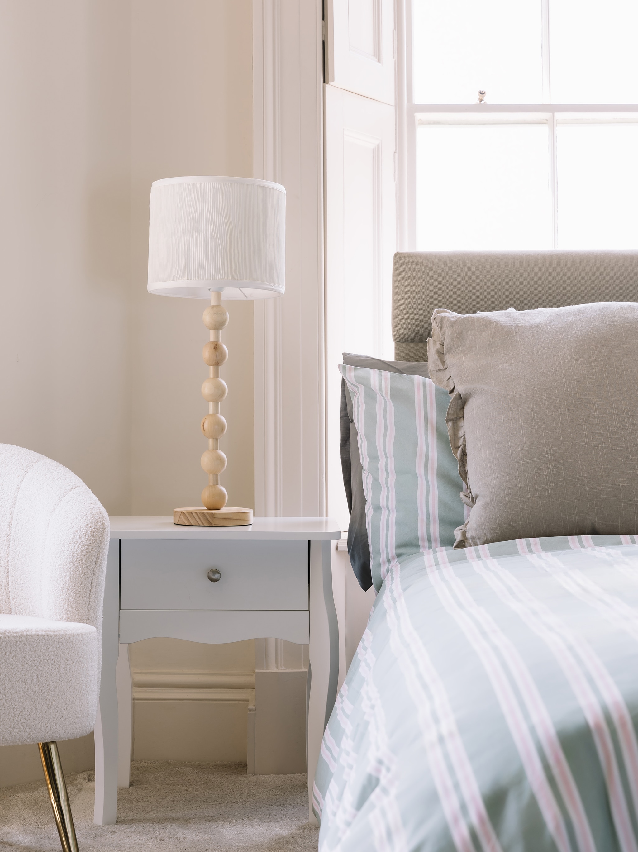 A white long legged bedside table with lamp on top