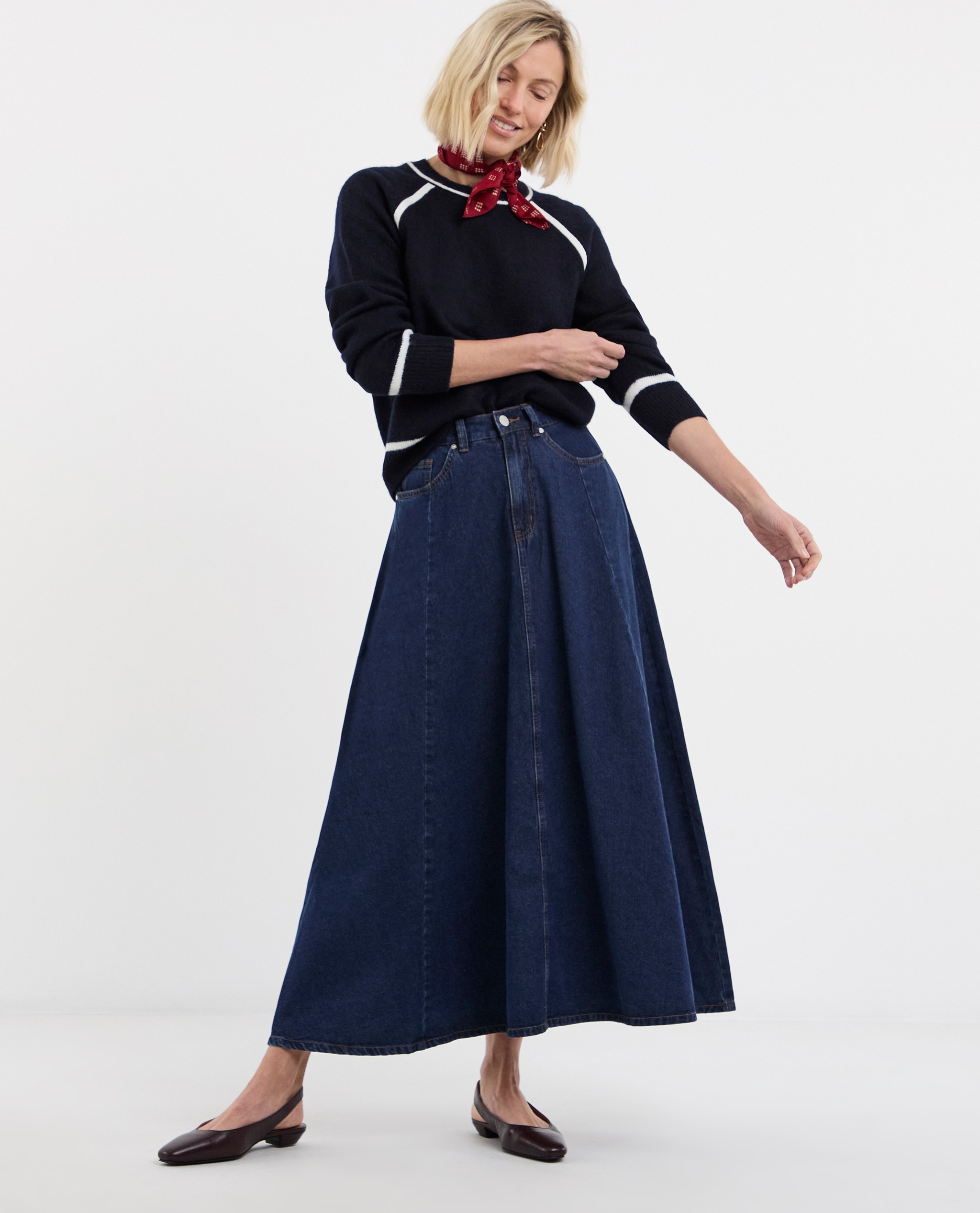 Model is wearing a contrast crew neck knitted jumper with a red patterned neck scarf and dark denim midi skirt.