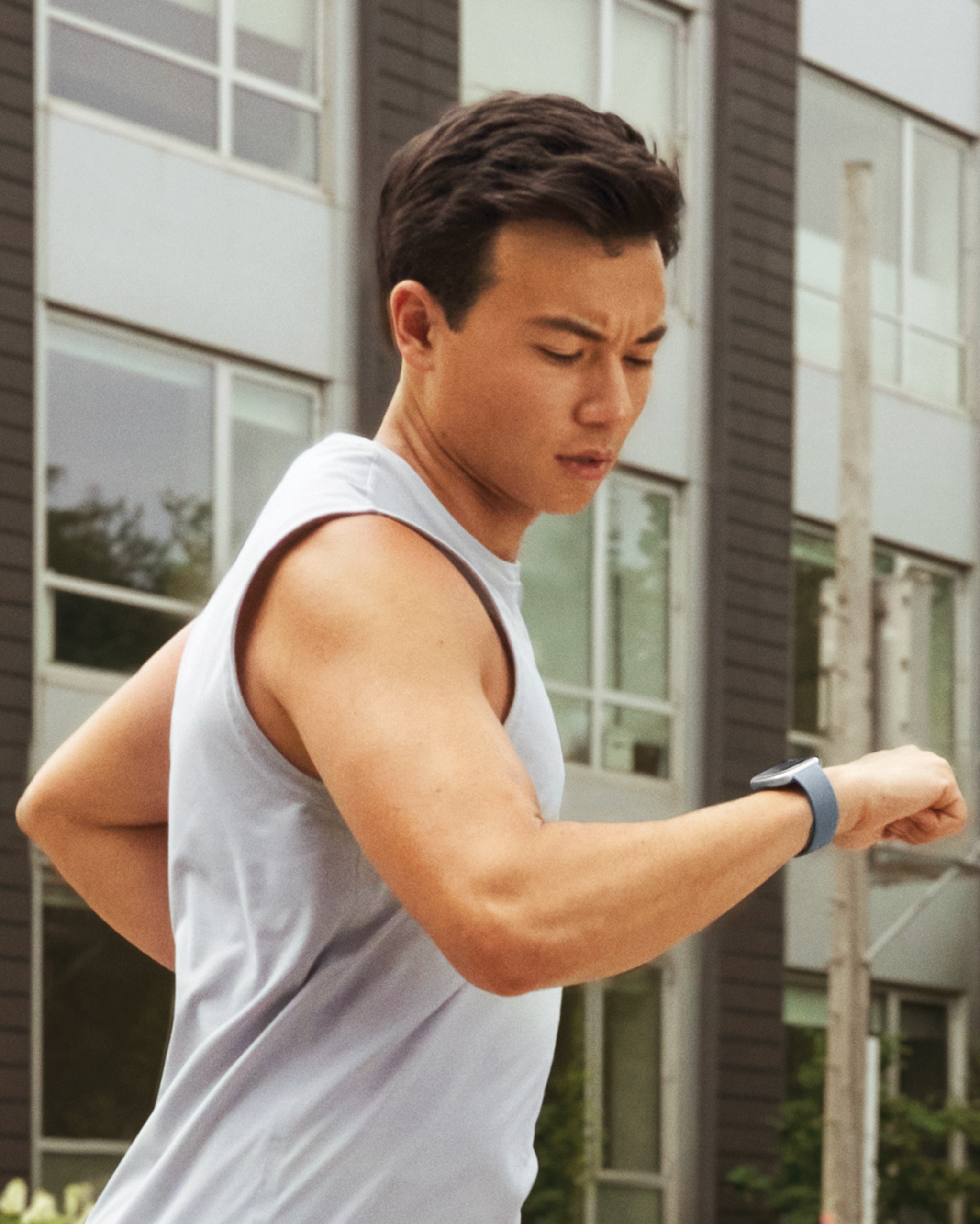 A man wearing a workout vest looking at his Fitbit watch