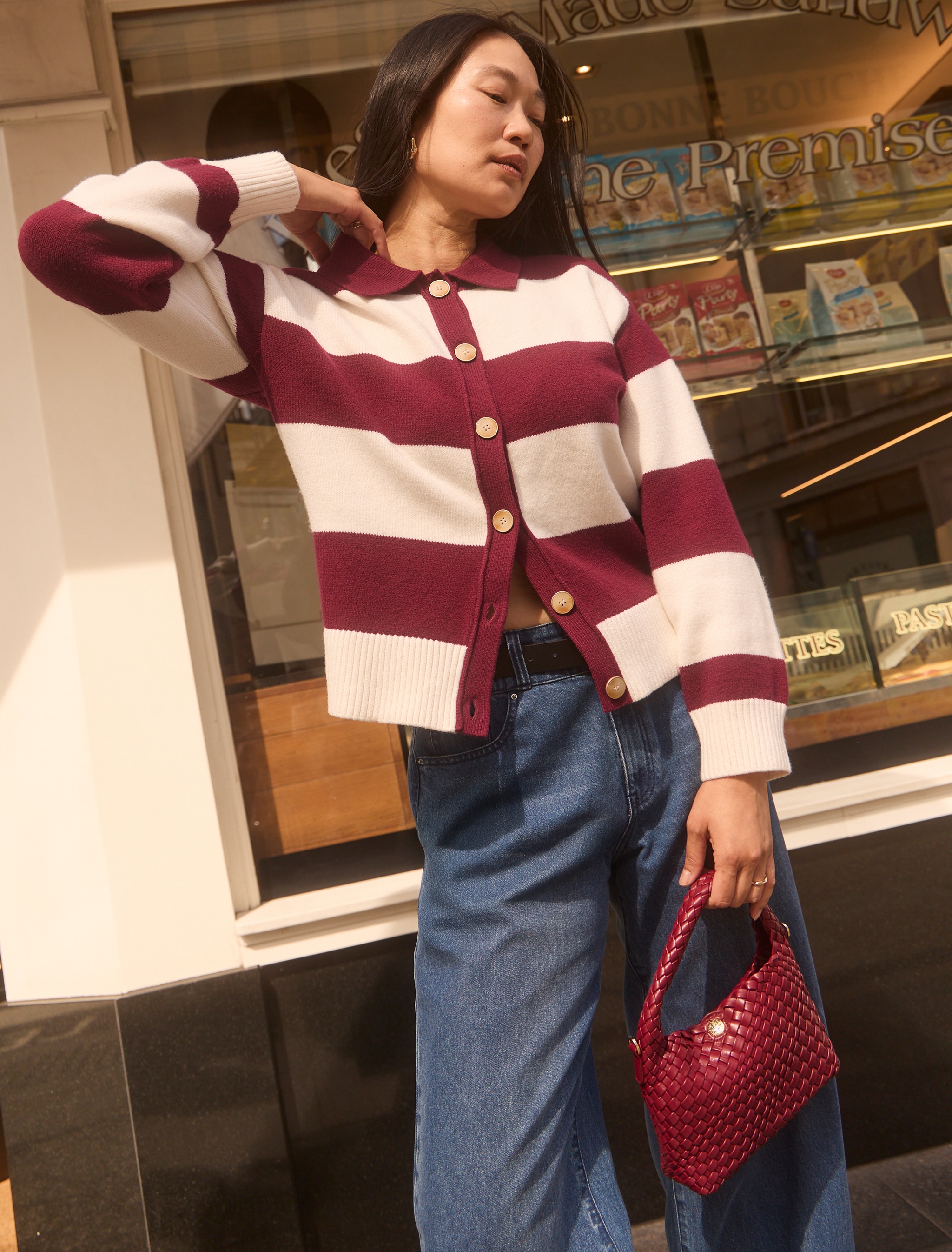 Lady wearing a maroon and cream hooped cardigan outside a shop.