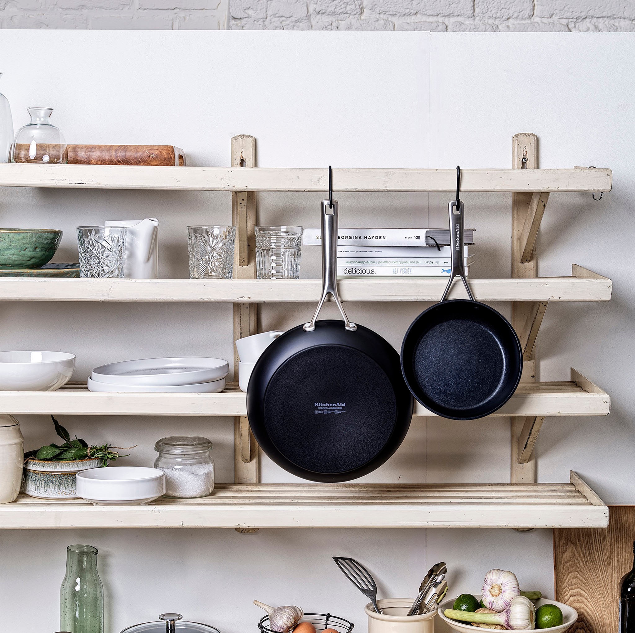 Two black frying pans hung up on a wooden shelf.