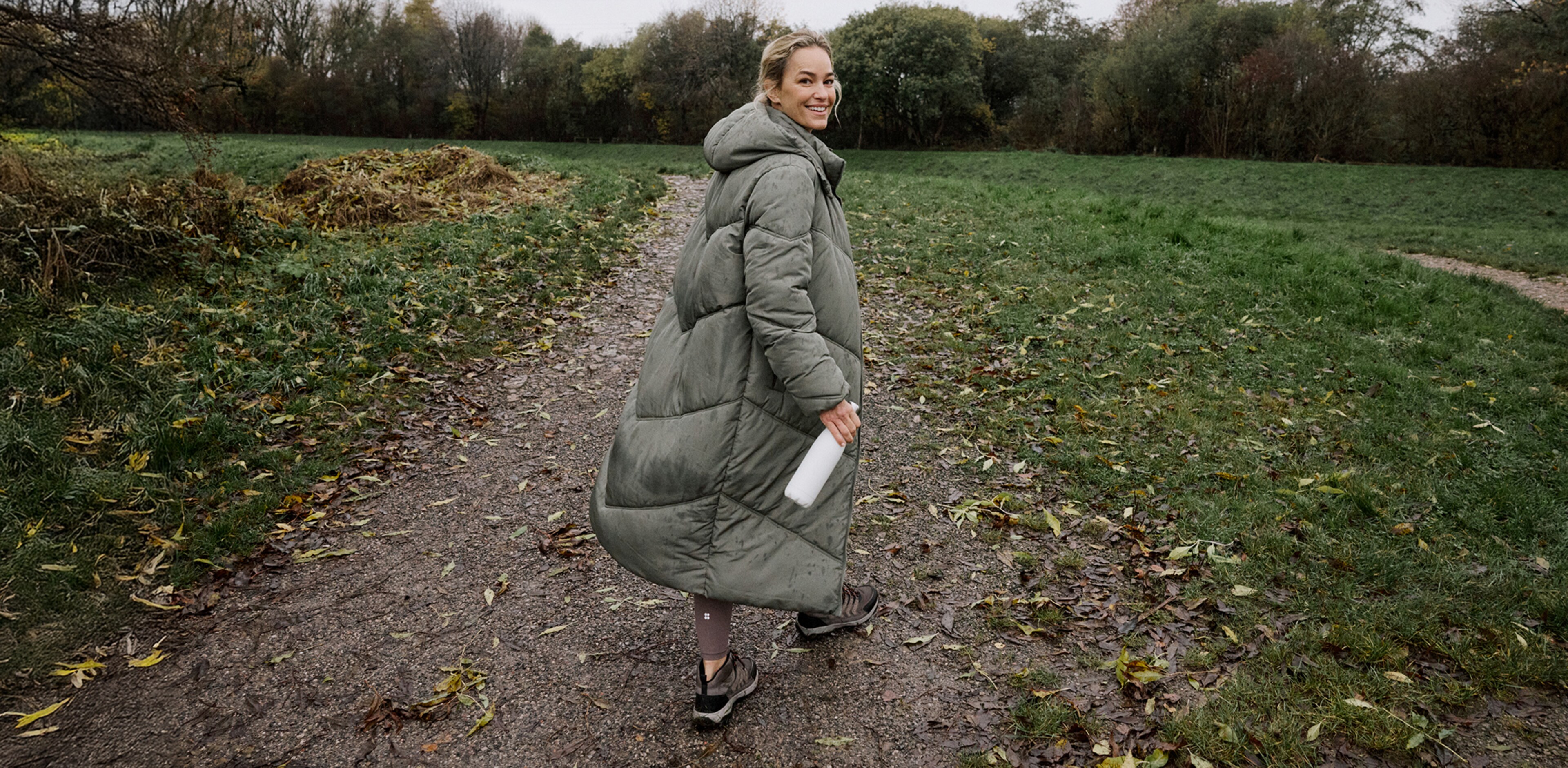 A lady outdoors walking wearing a long green quilted coat.