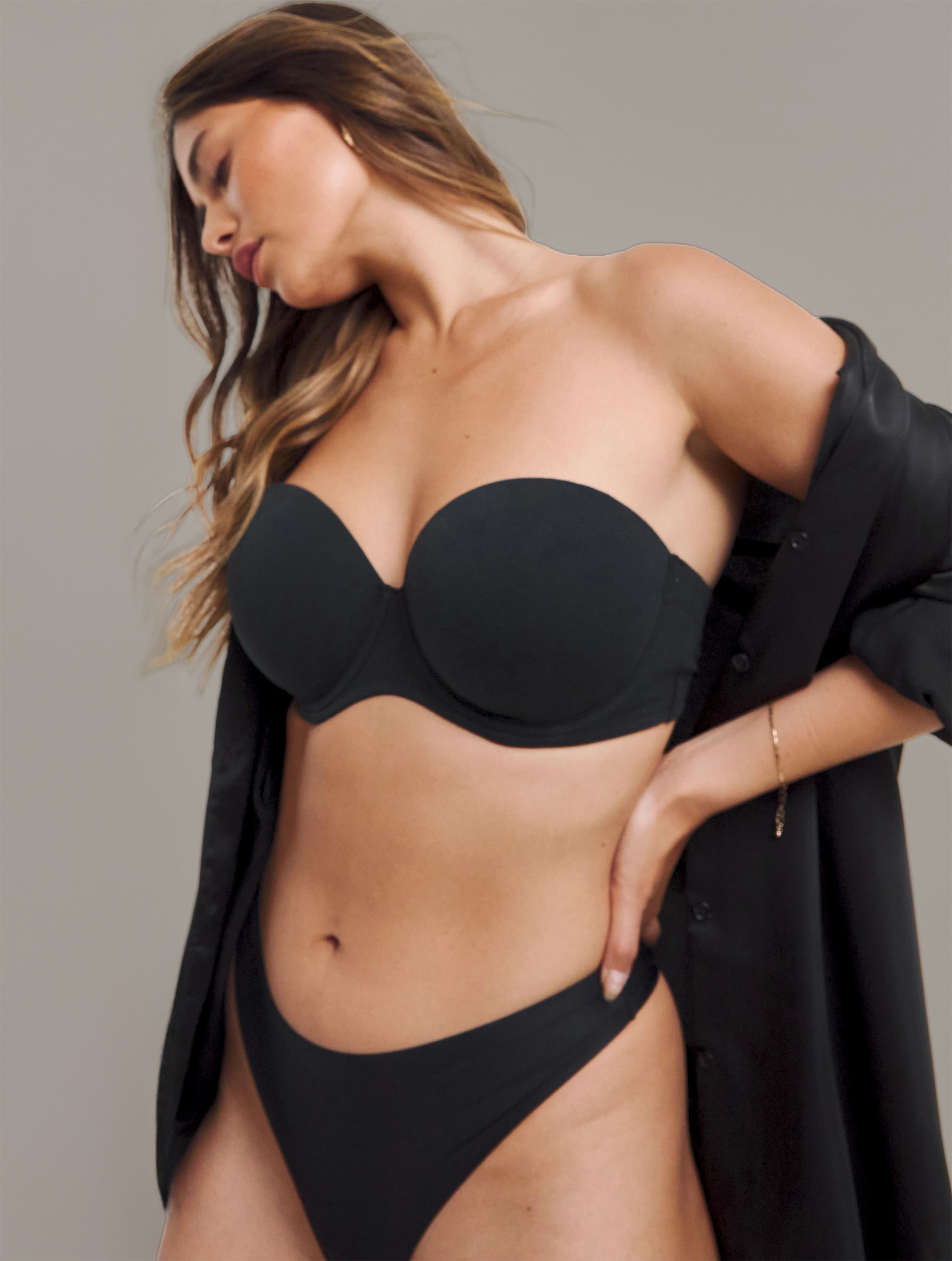 A lady stood looking to the left wearing a black strapless bra.