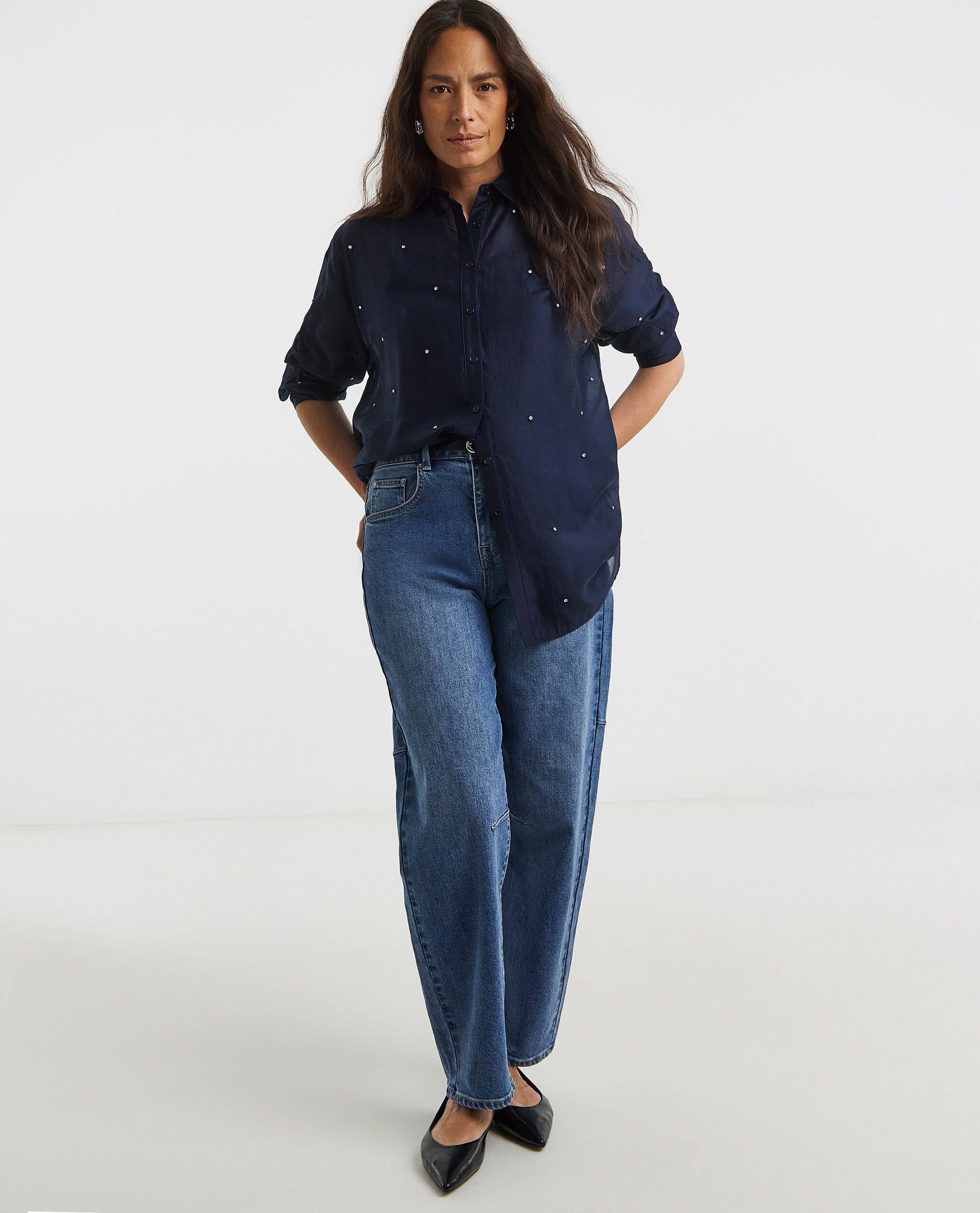 Model is wearing a navy embellished long sleeve shirt with blue denim jeans.