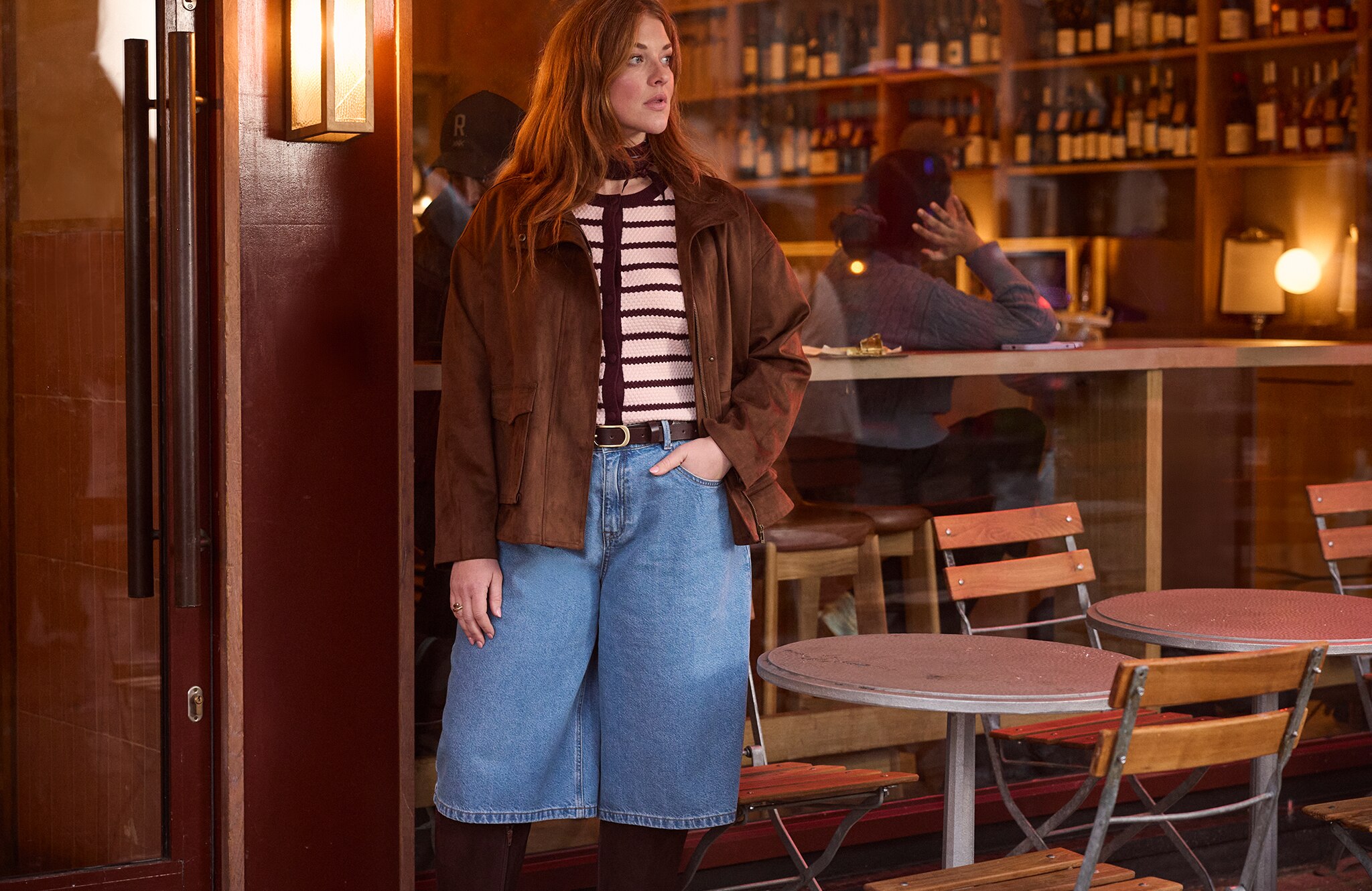 Model is wearing a textured stripe short sleeve cardigan with a tan suedette funnel neck relaxed fit jacket with mid blue denim jorts and tan boots.