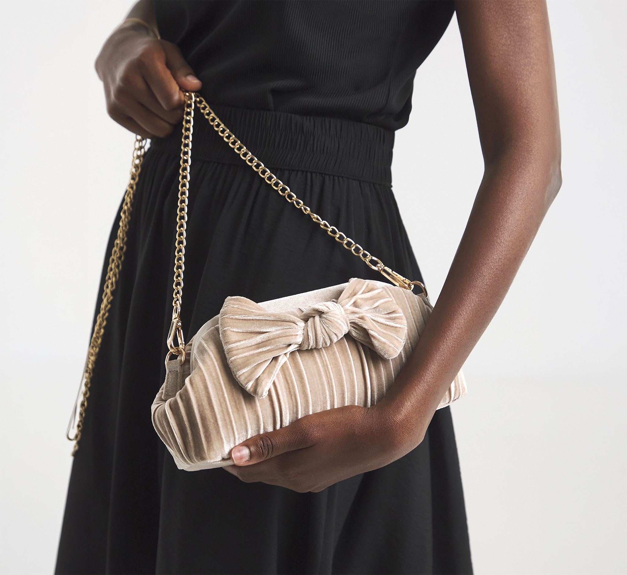 A close up of a lady wearing a black dress holding a velvet bow pleated clutch bag