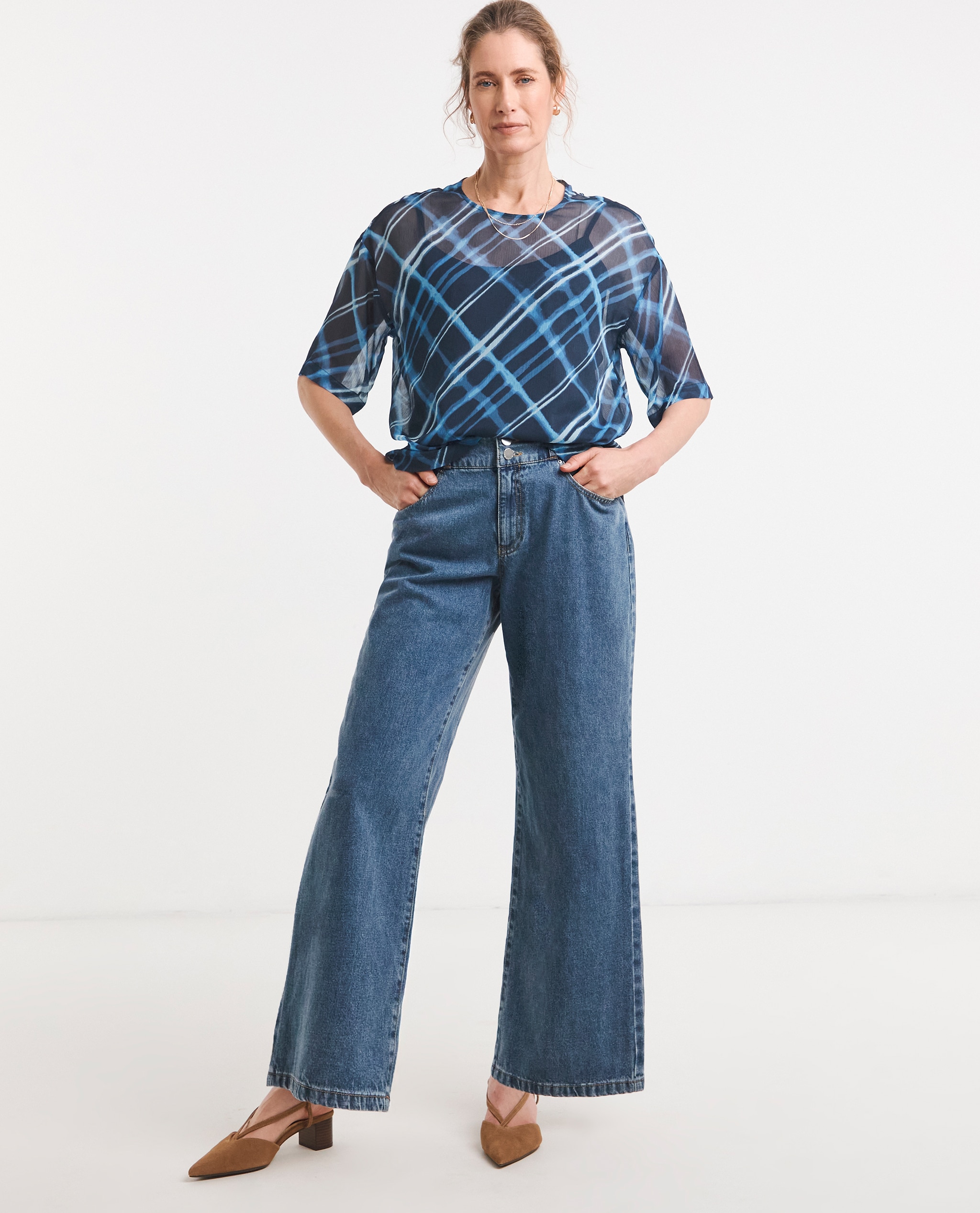 Model is wearing a blue check chiffon short sleeve boxy top with a pair of blue flared denim jeans with low heel pointed toe leather slingback shoes in camel.