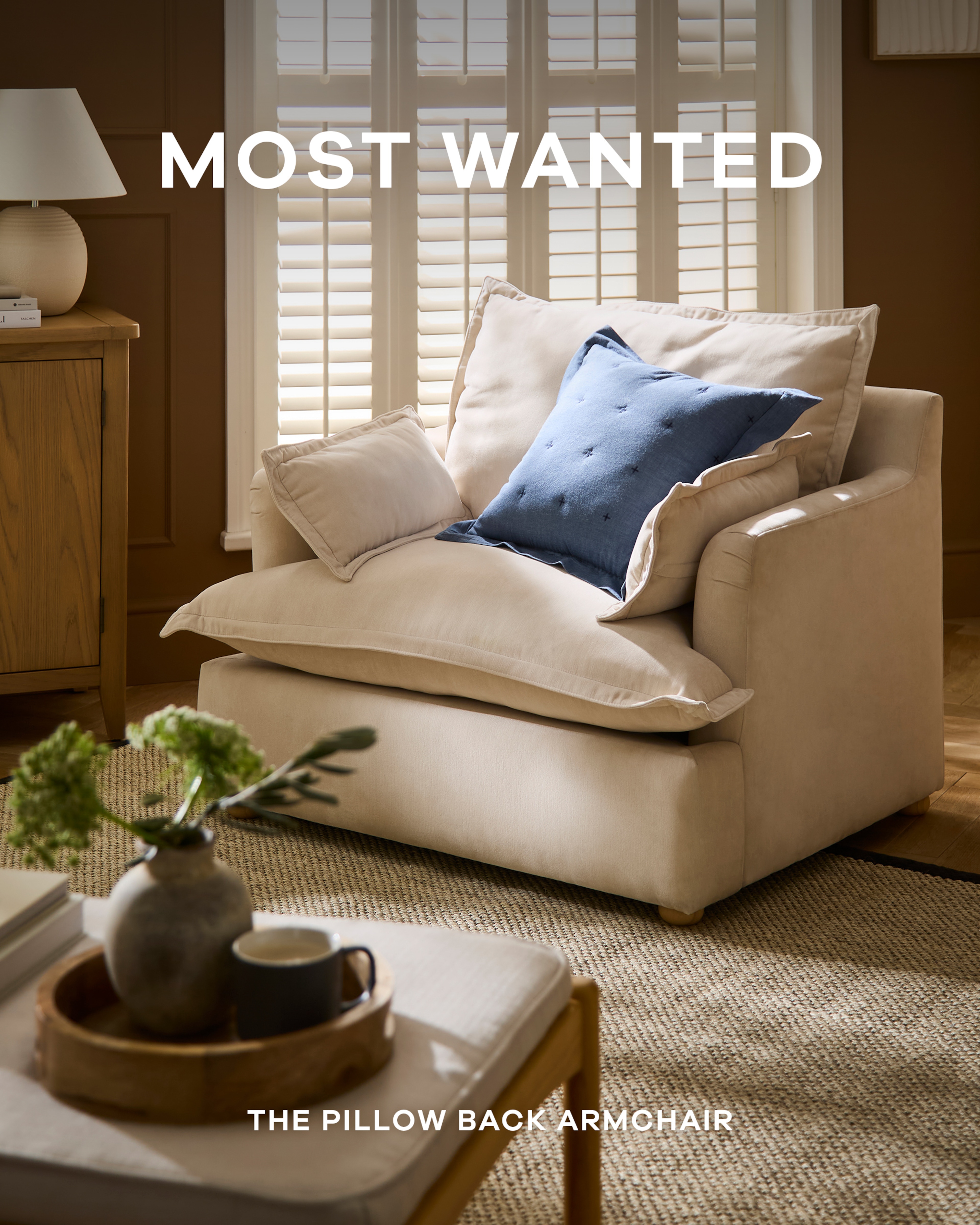 A creamy stone coloured pillowback armchair with a blue cushion on it in a living room scene.