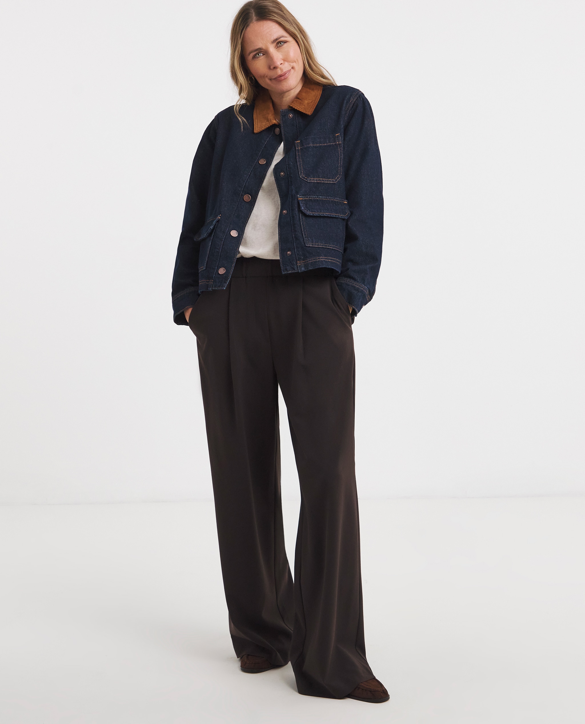 Model is wearing a indigo cord collar barn jacket with a white t-shirt and black trousers and loafers.