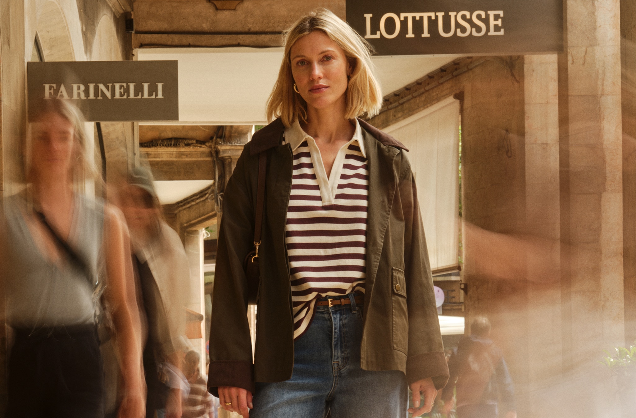 Lady wearing a stripe top with brown jacket walking near shops