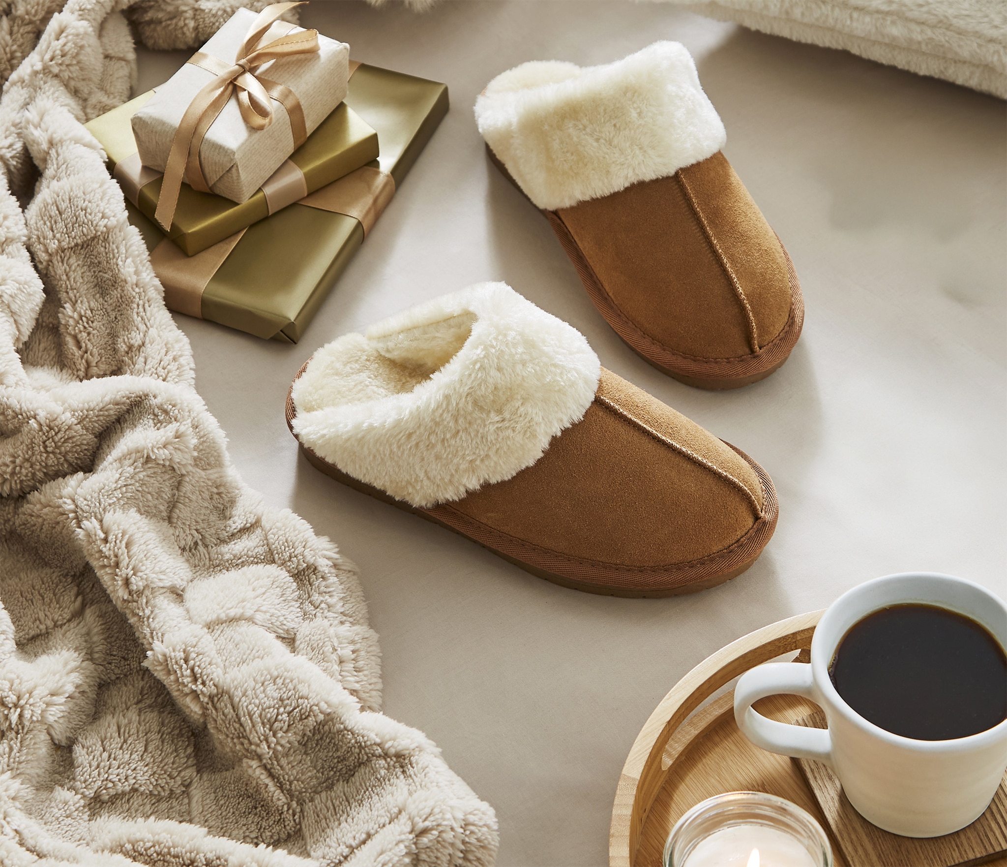 A pair of brown suede mule slippers next to some gifts and a tray with coffee