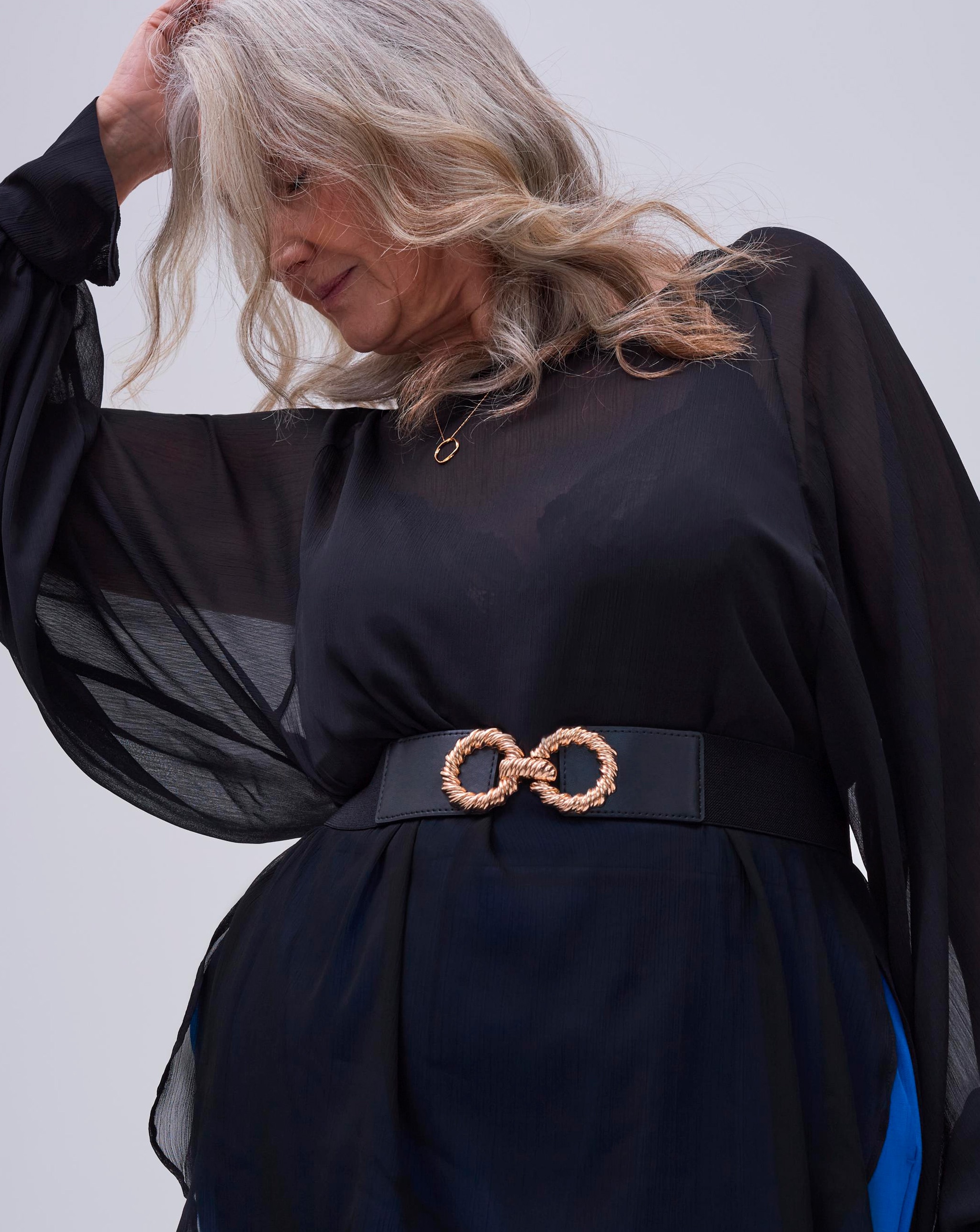 Model wearing black blouse and black belt with gold detailed buckle