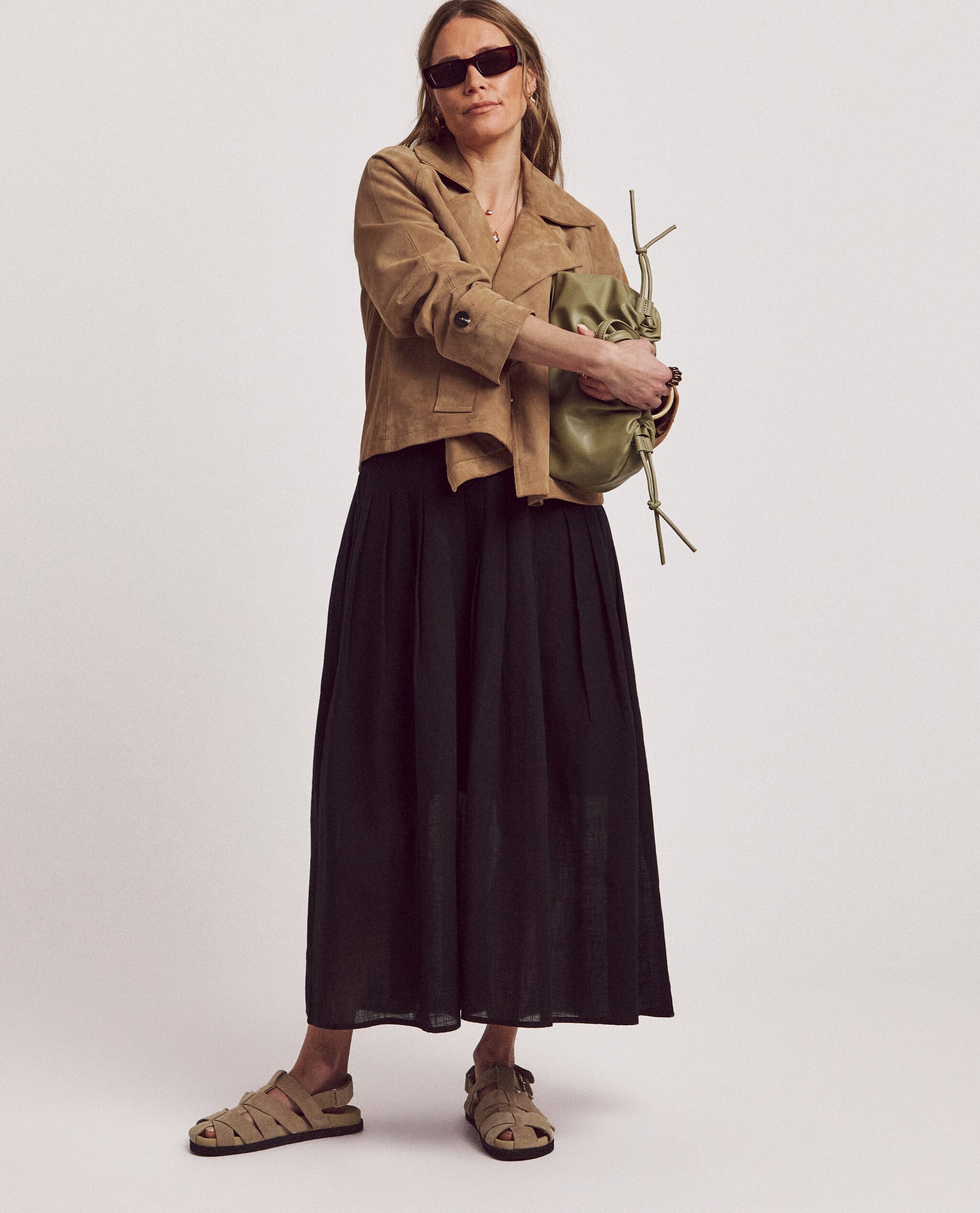 Model is wearing a camel suedette jacket with a black pleat tuck midi skirt and camel sandals.