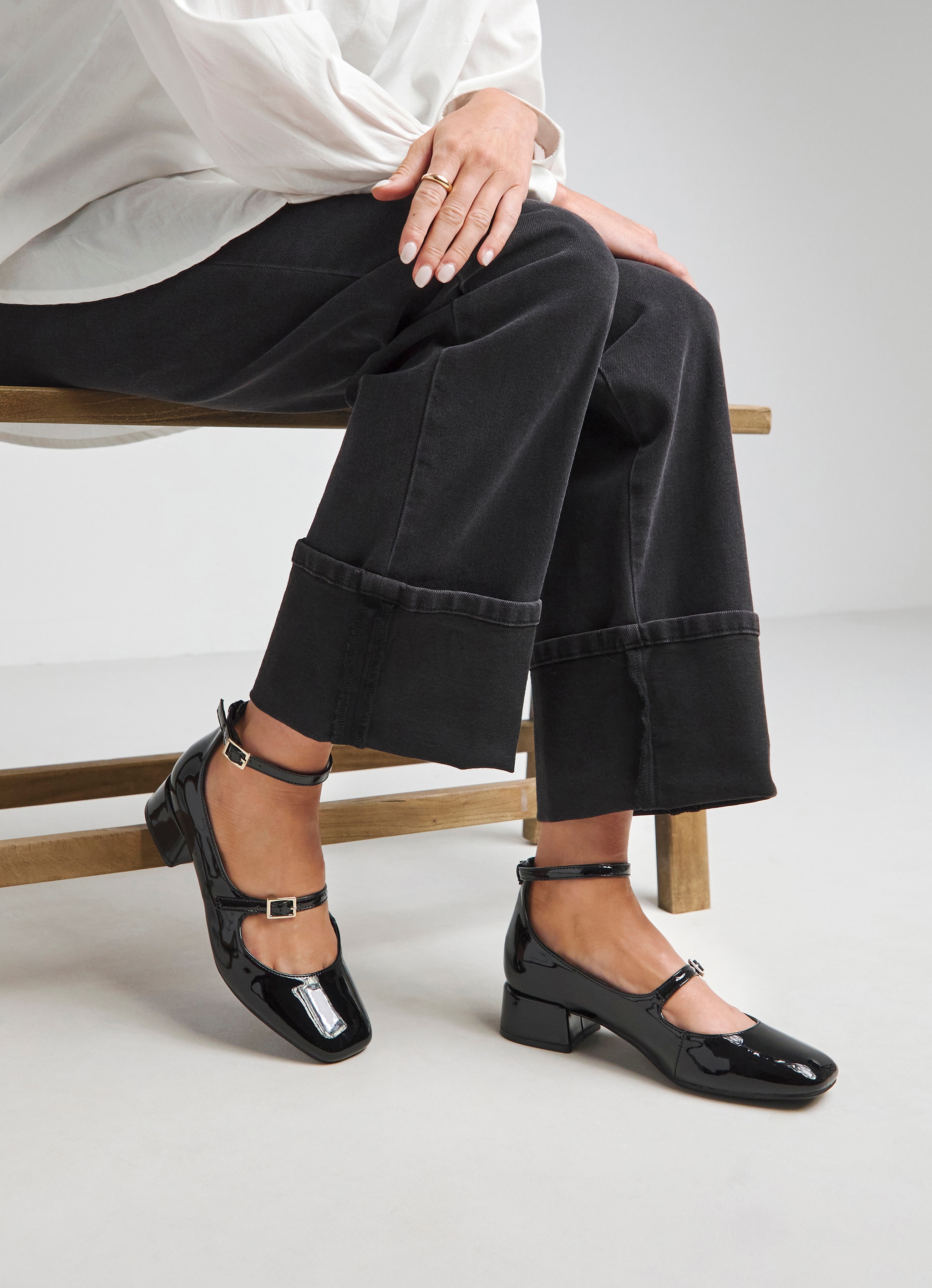 A person sat on a wooden bench wearing black denim jeans with black patent Mary Jane shoes