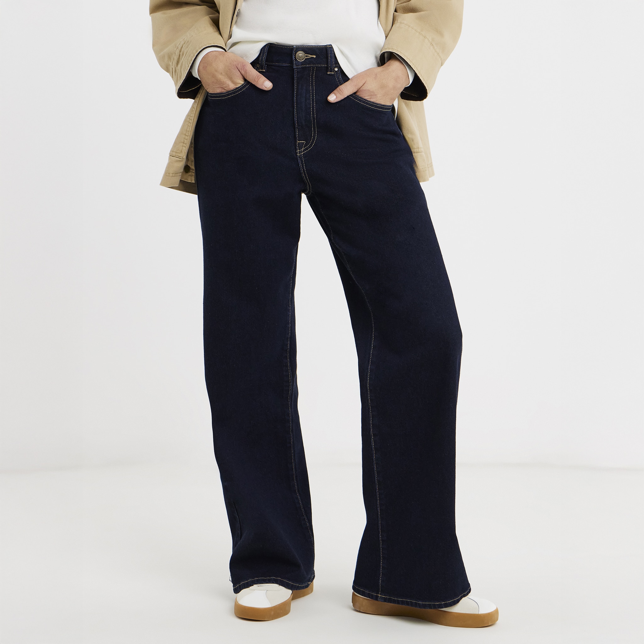 A person wearing indigo coloured jeans with white trainers.