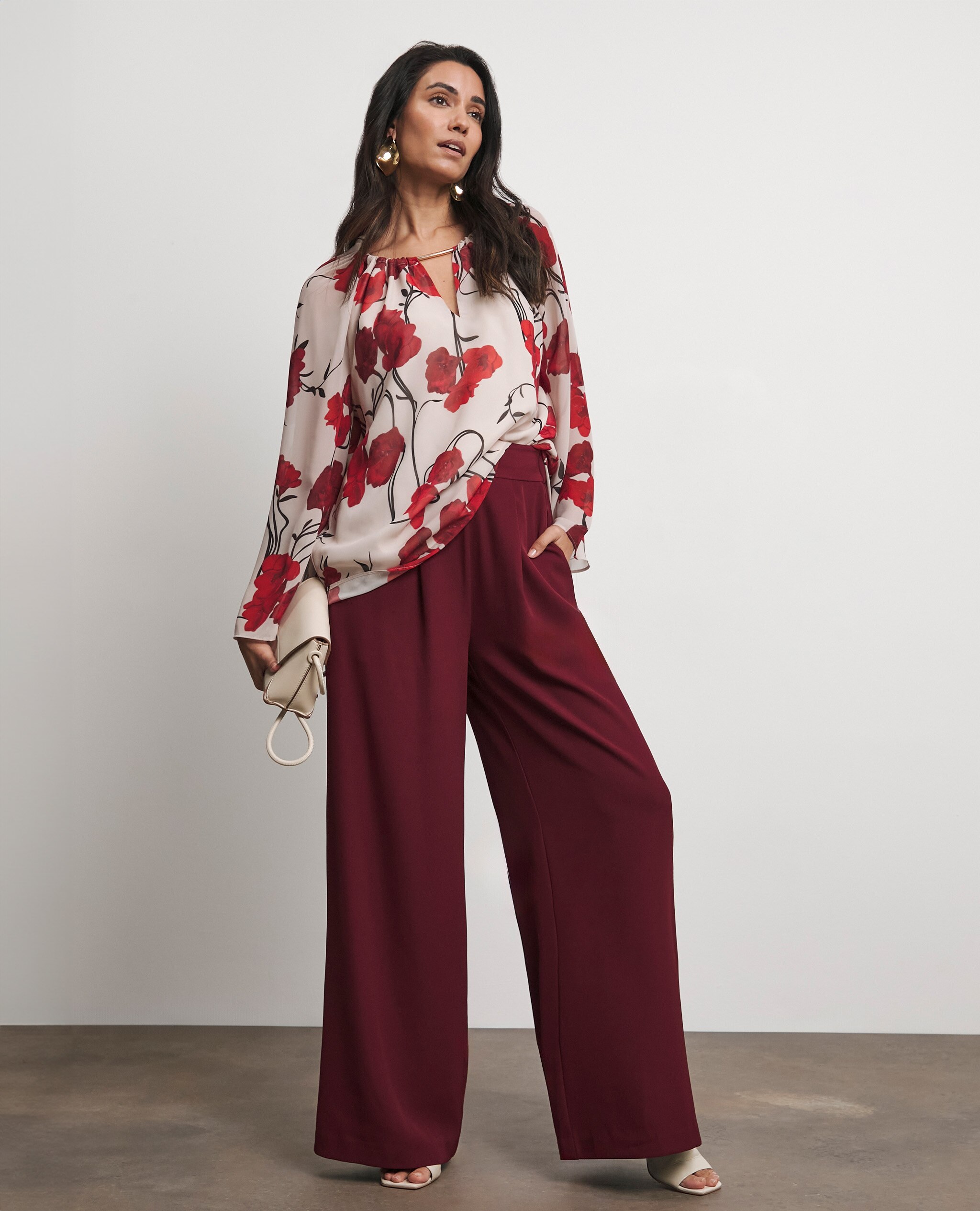 Model wearing burgundy trousers with a patterned long sleeve top