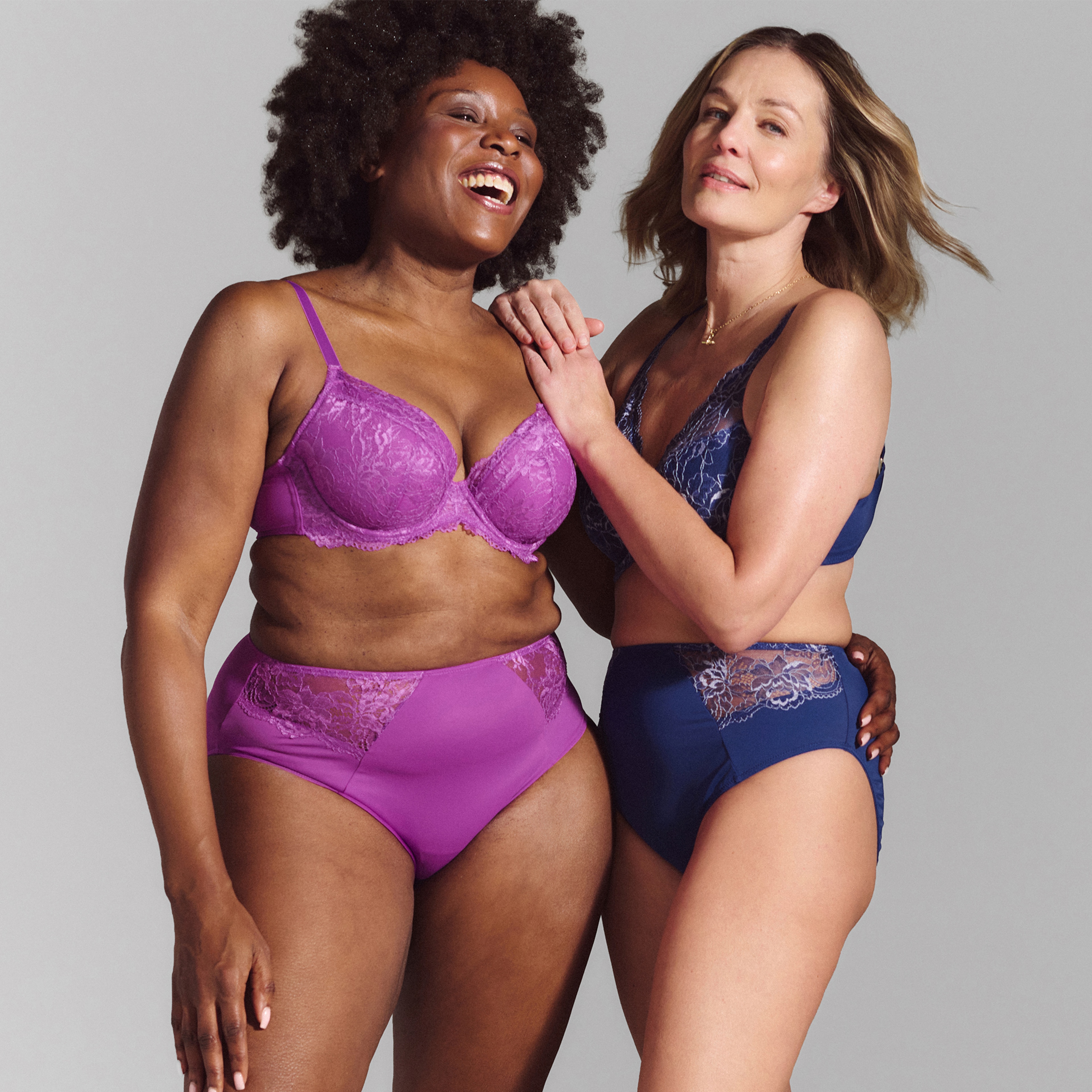 Two women stood wearing pink and blue lingerie sets.