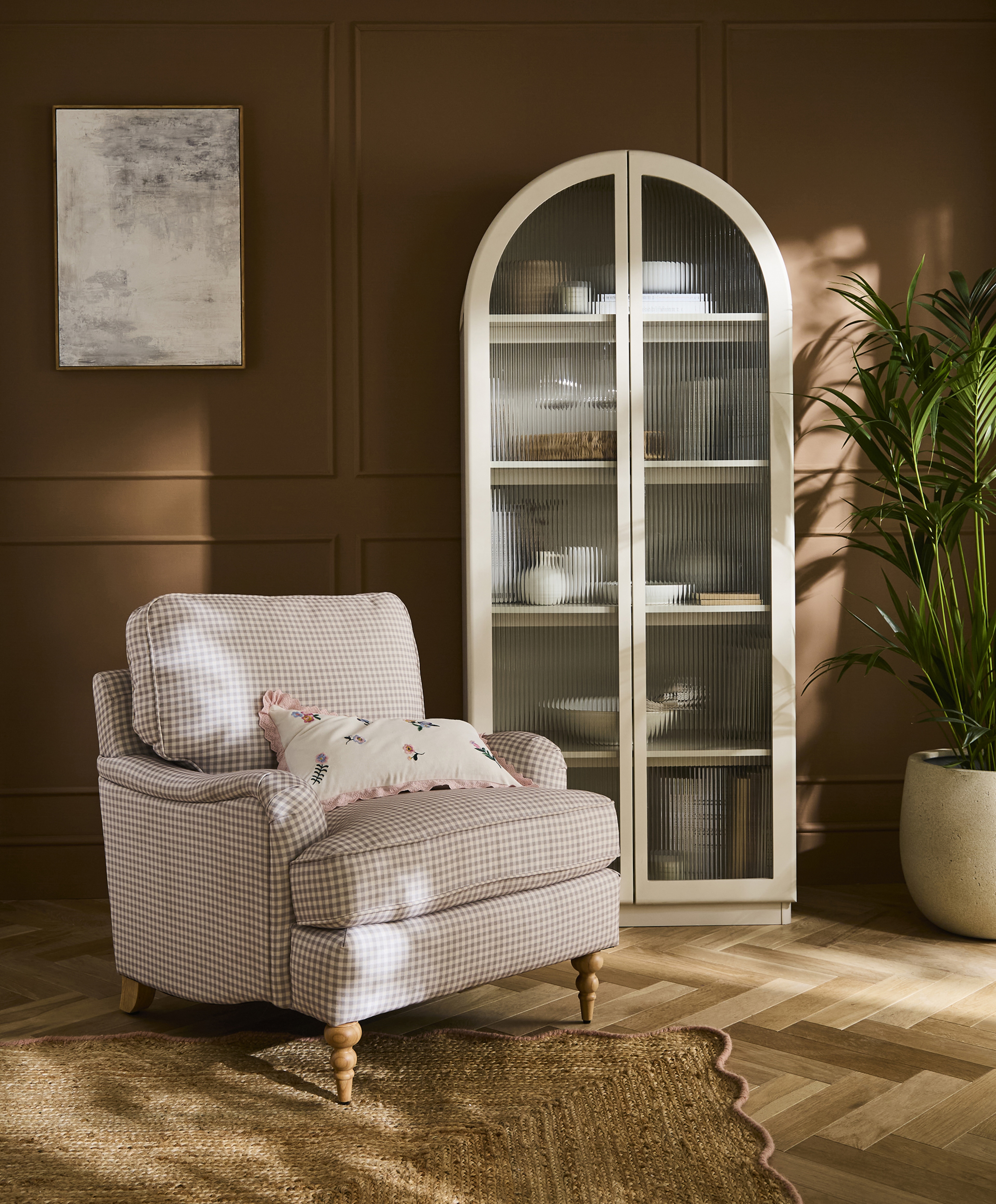 A pink and white check armchair in a room with cabinet with glass windows