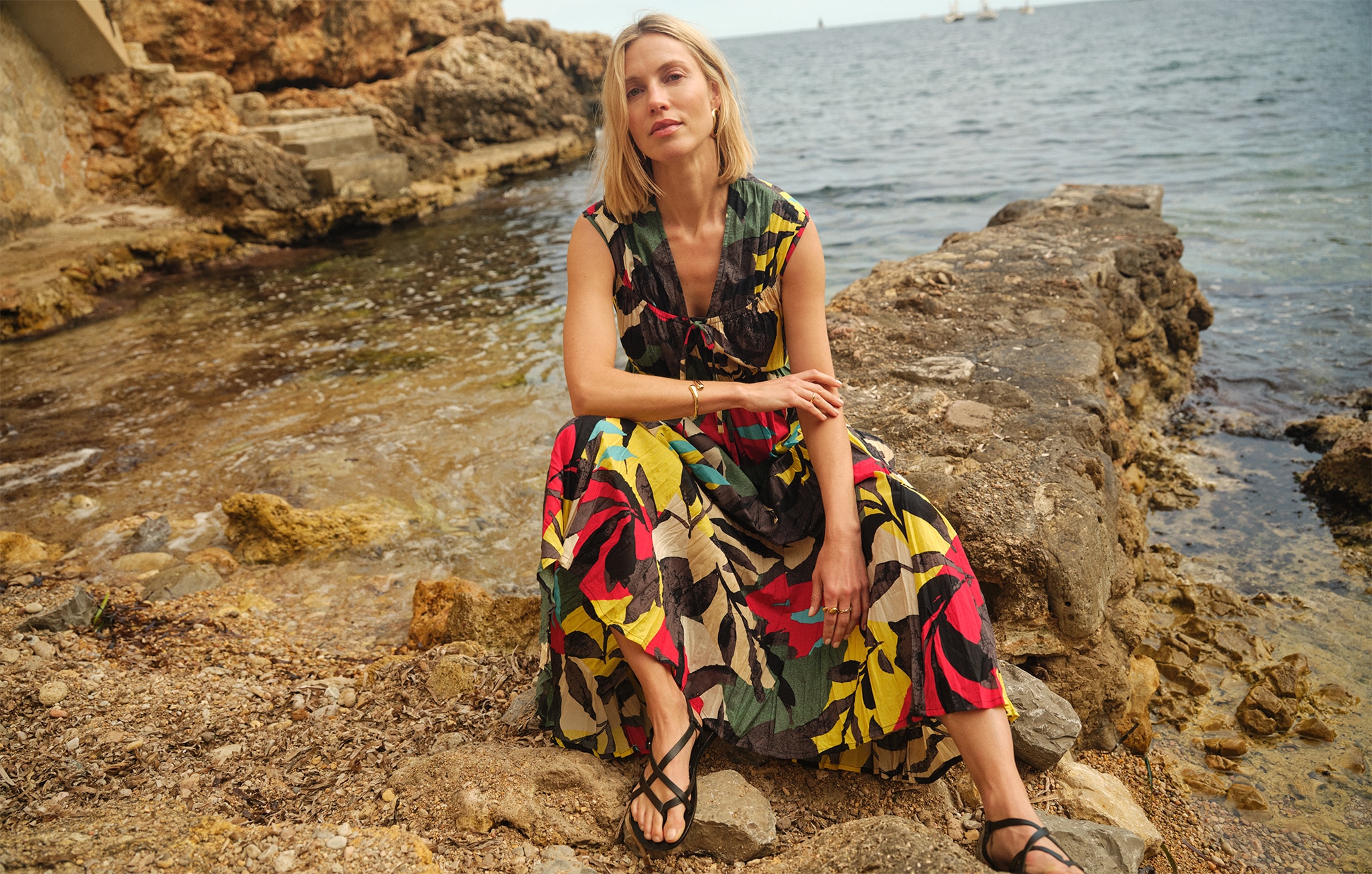 Lady in a colourful dress sat on rocks next to the sea