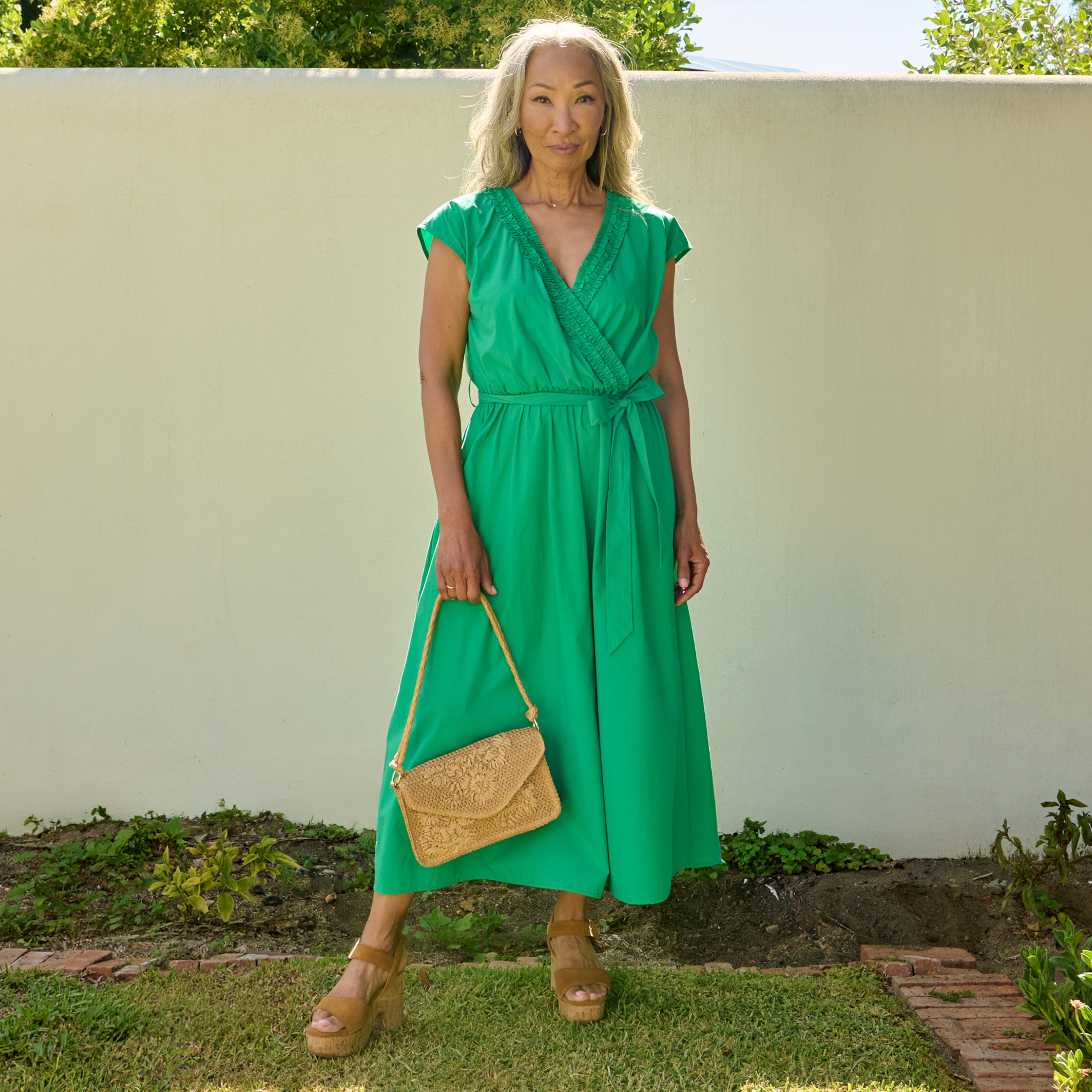 A lady wearing a green dress holding a light brown hand bag