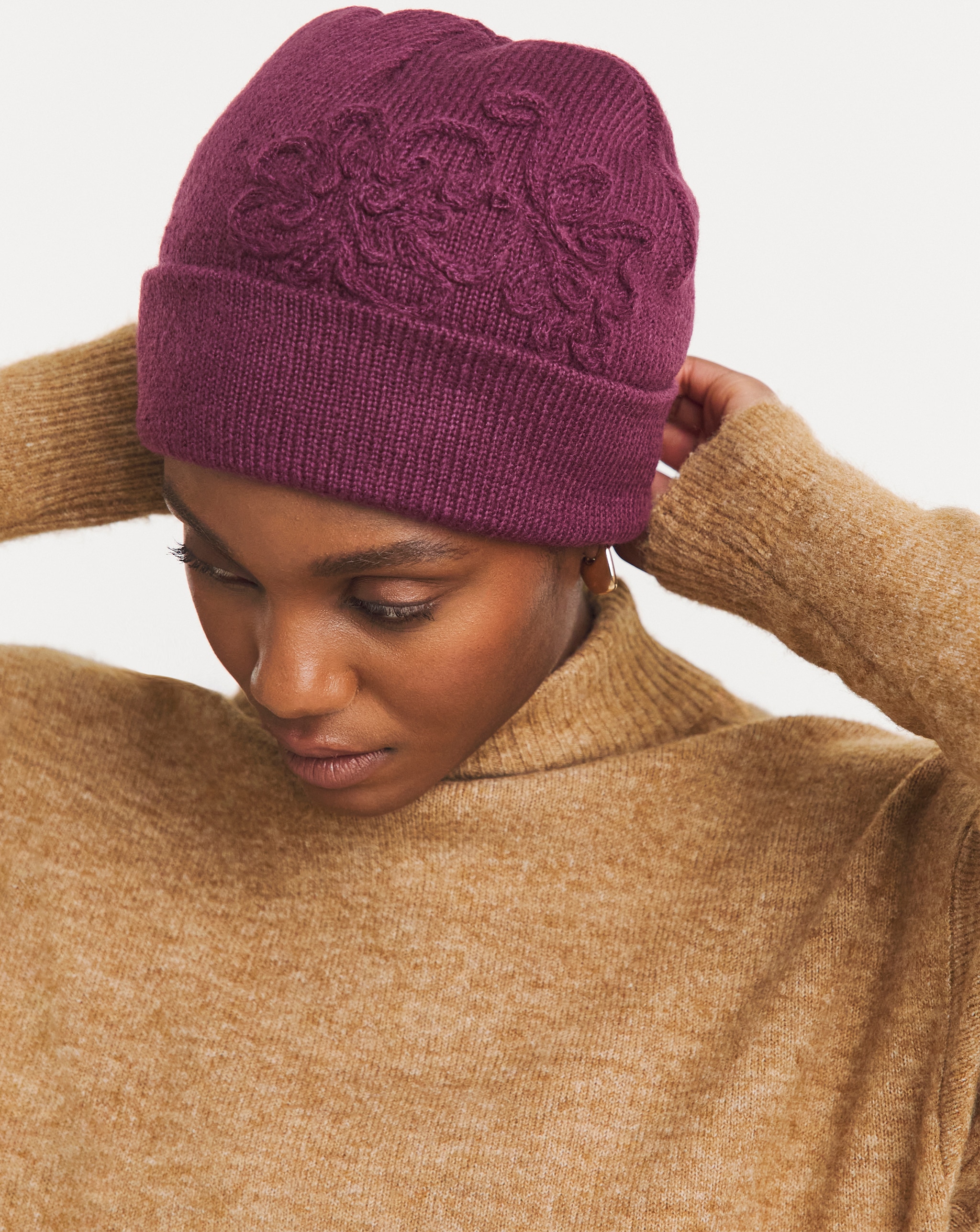 Person wearing a plum-coloured floral embroidered beanie and a light brown jumper.