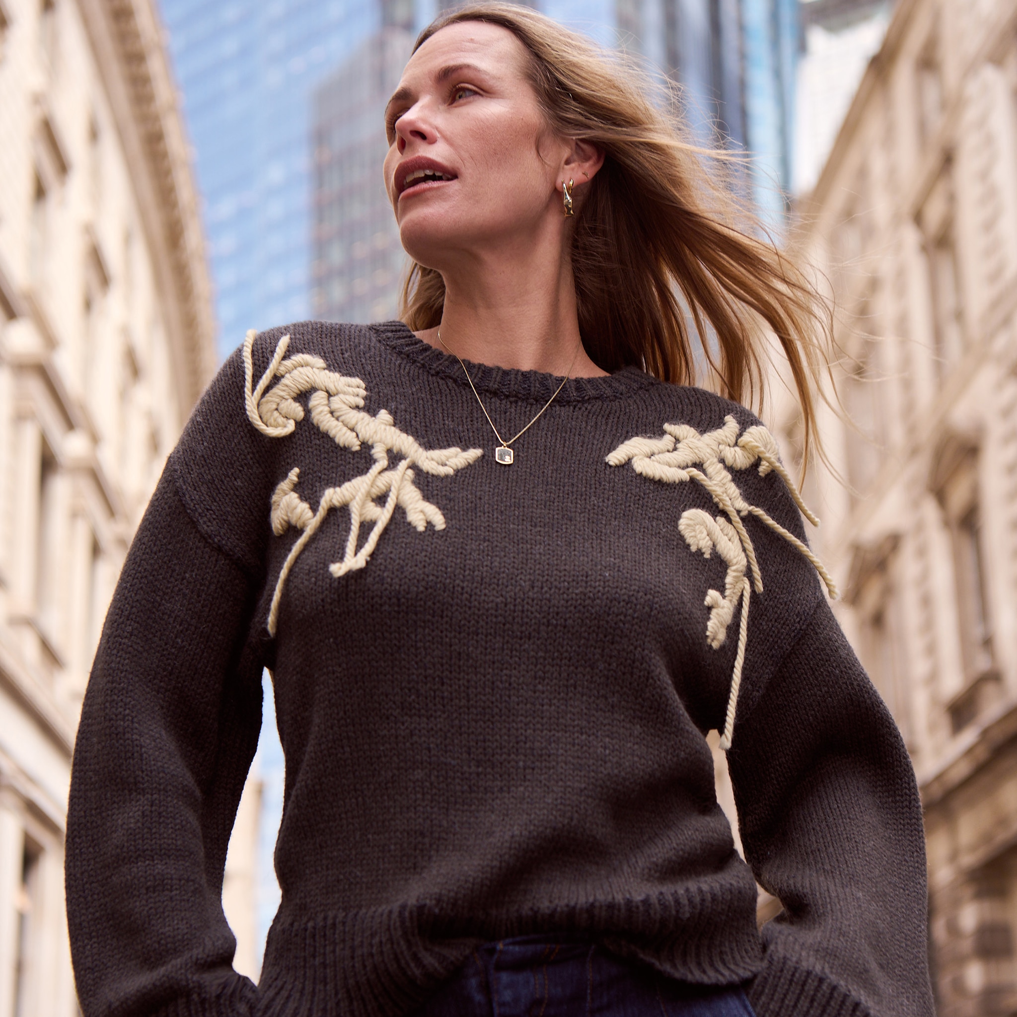 A lady wearing a charcoal jumper with gold leafy pattern on the shoulders.