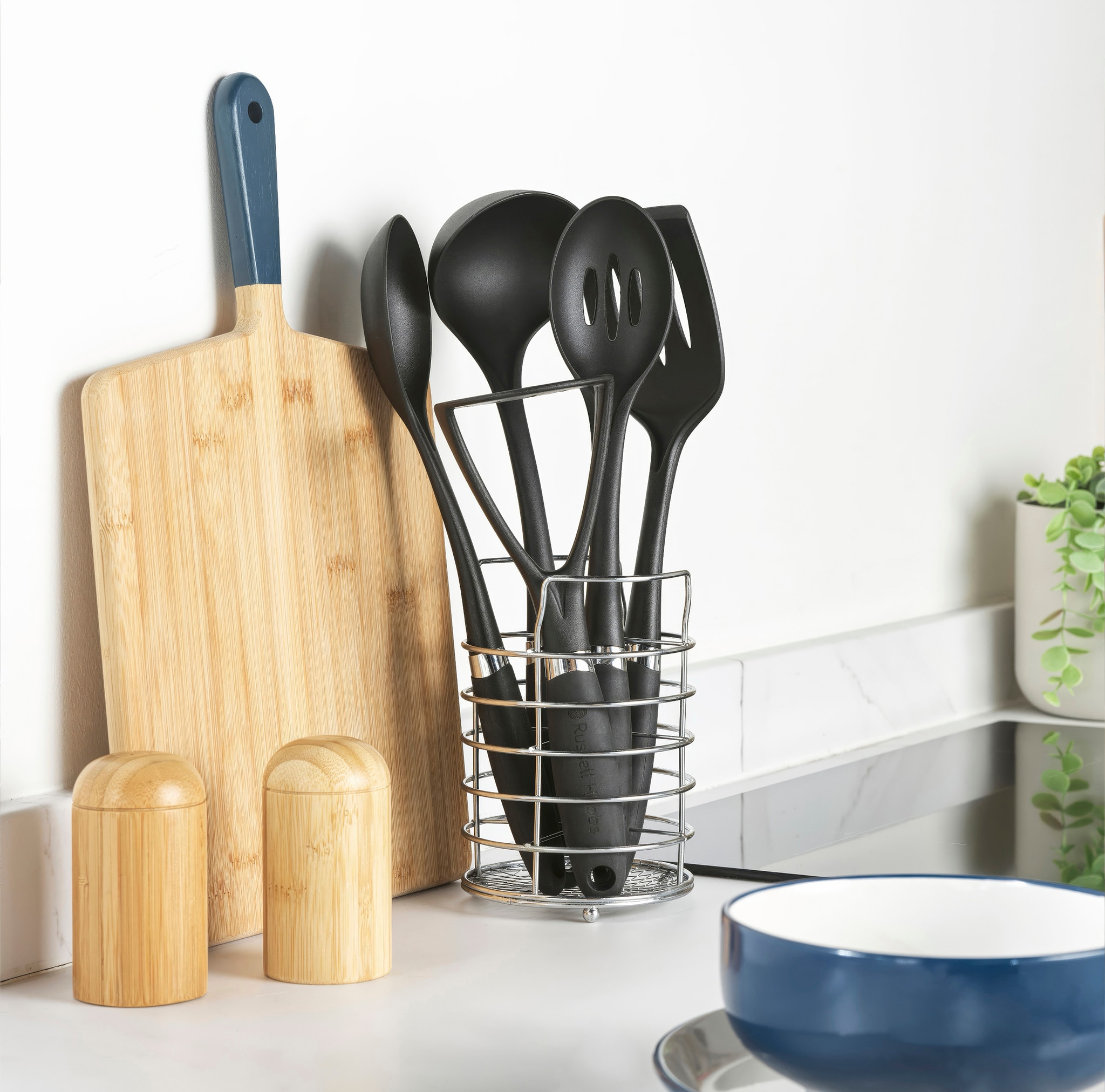 A range of black kitchen utensils in a chromed wire storage container.