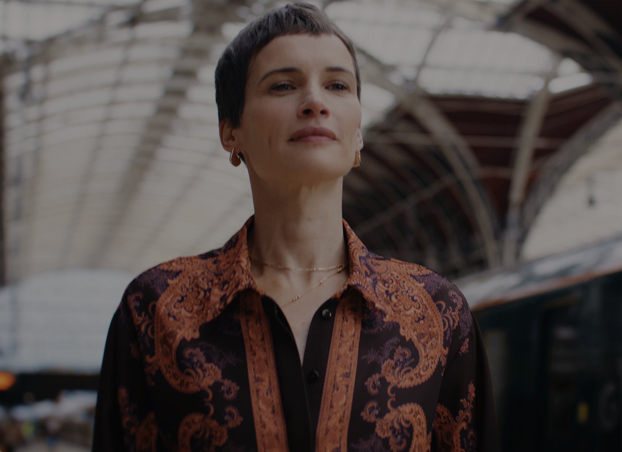 A lady walking through a train station wearing a black and orange printed co-ord outfit