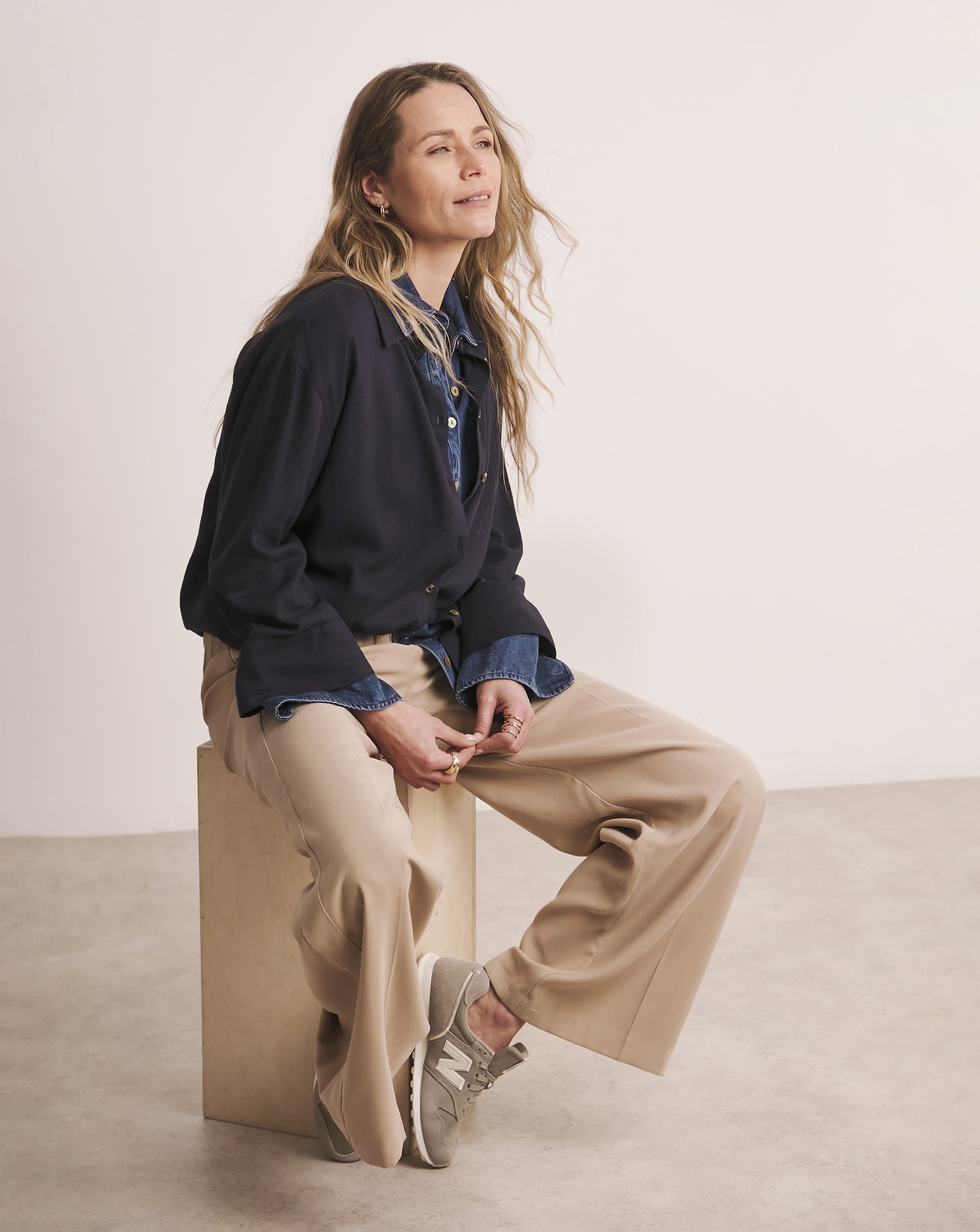 A lady sat on a box wearing stone coloured wide leg trousers.