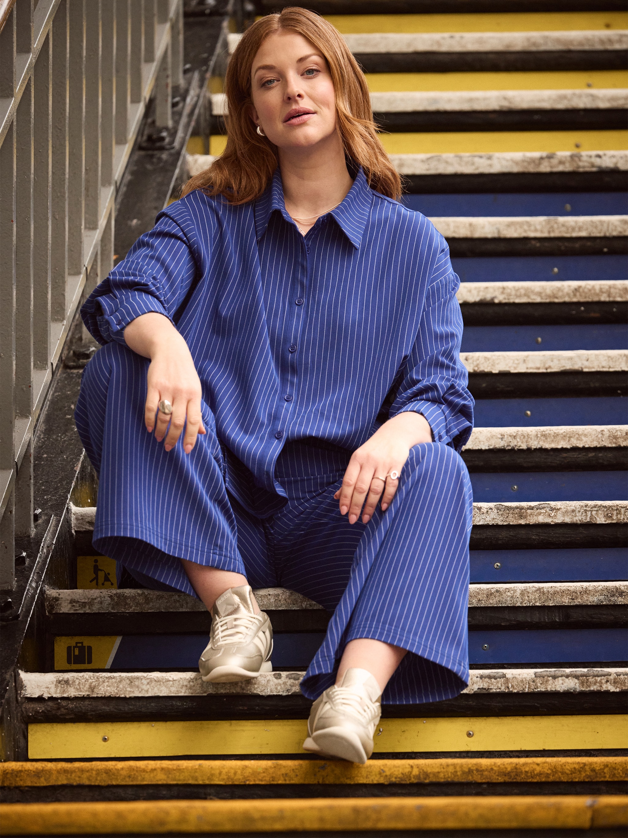 A lady sat on some stairs wearing a blue outfit with white pin stripes